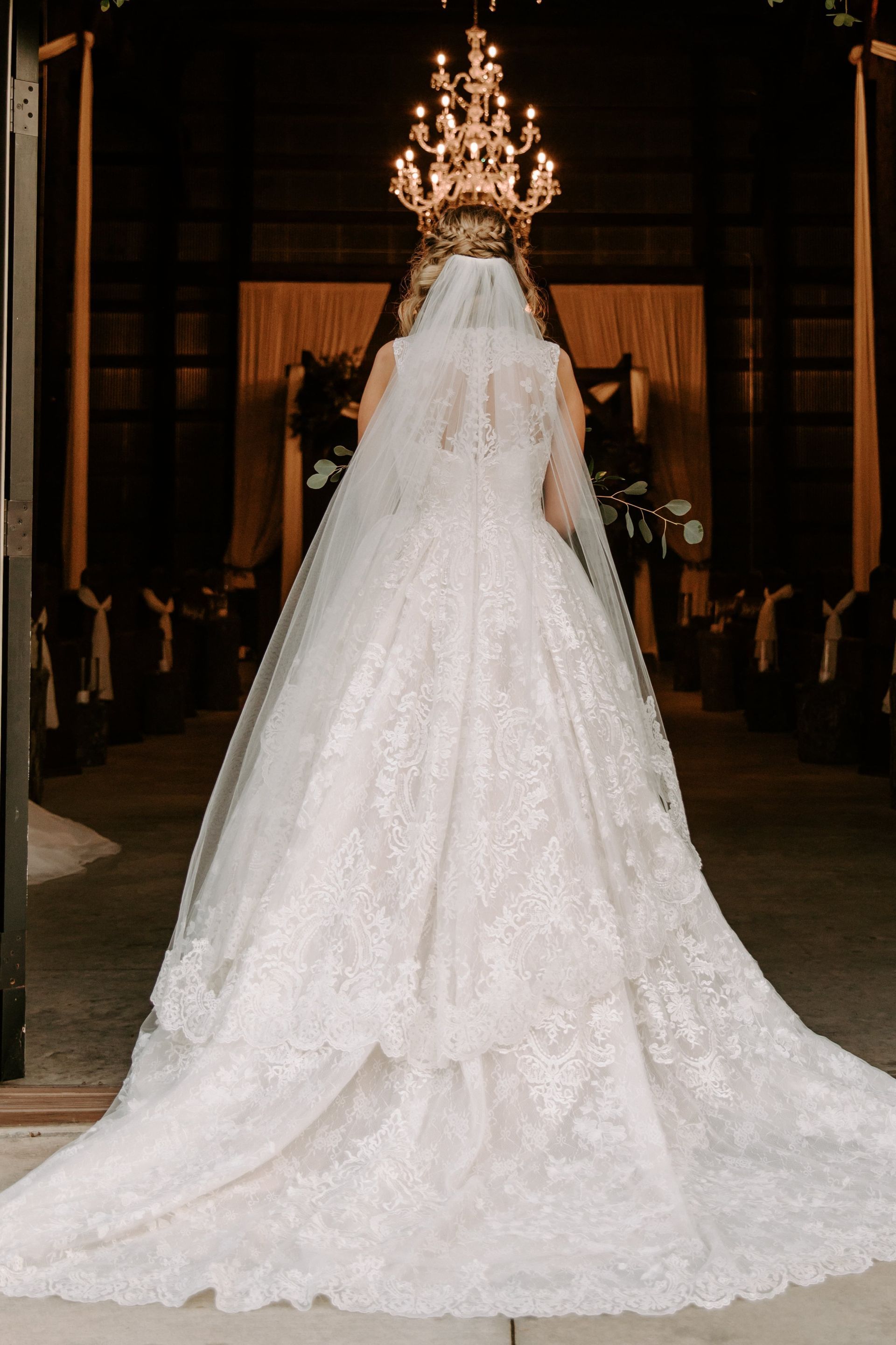 White wedding gown with a long train displayed under a chandelier in a dimly lit venue
