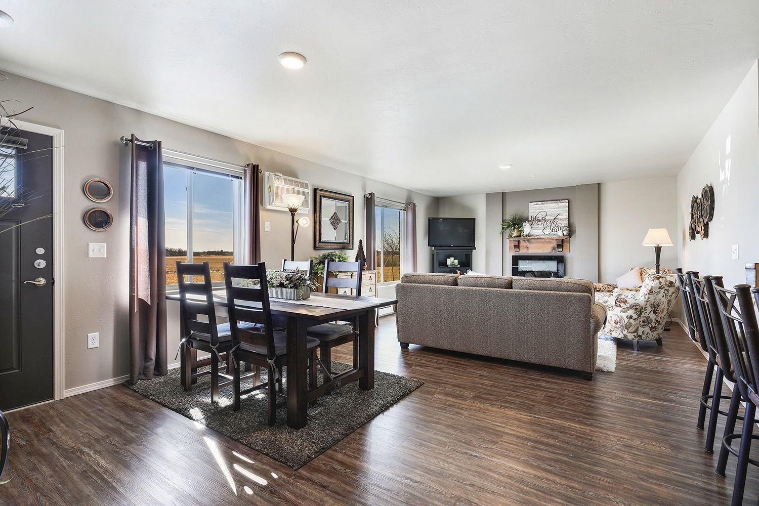 Open-plan living and dining room with dark wood floors, gray sofa, and black dining table near a bright window
