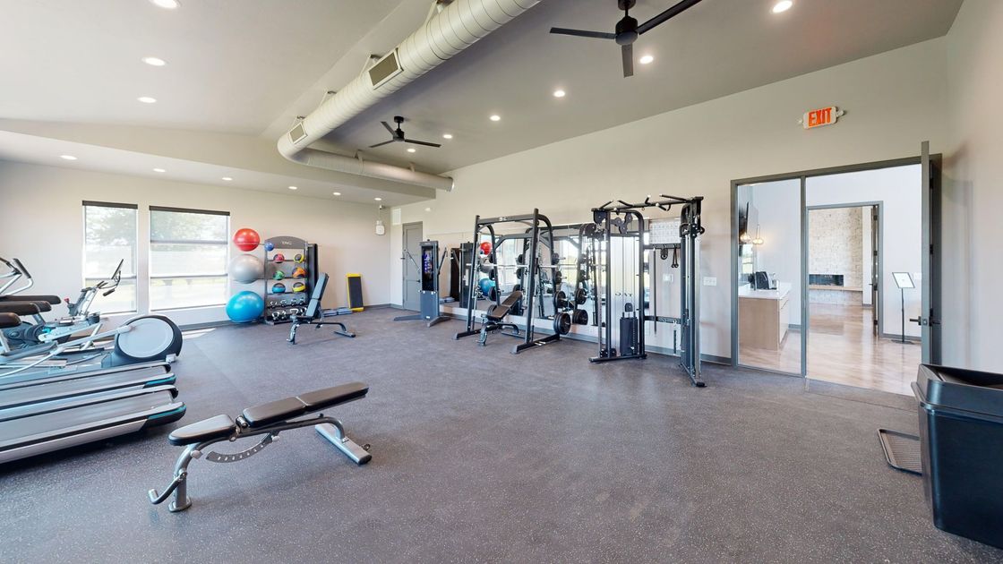 Bright gym interior with exercise machines, weights, and a bench on a carpeted floor