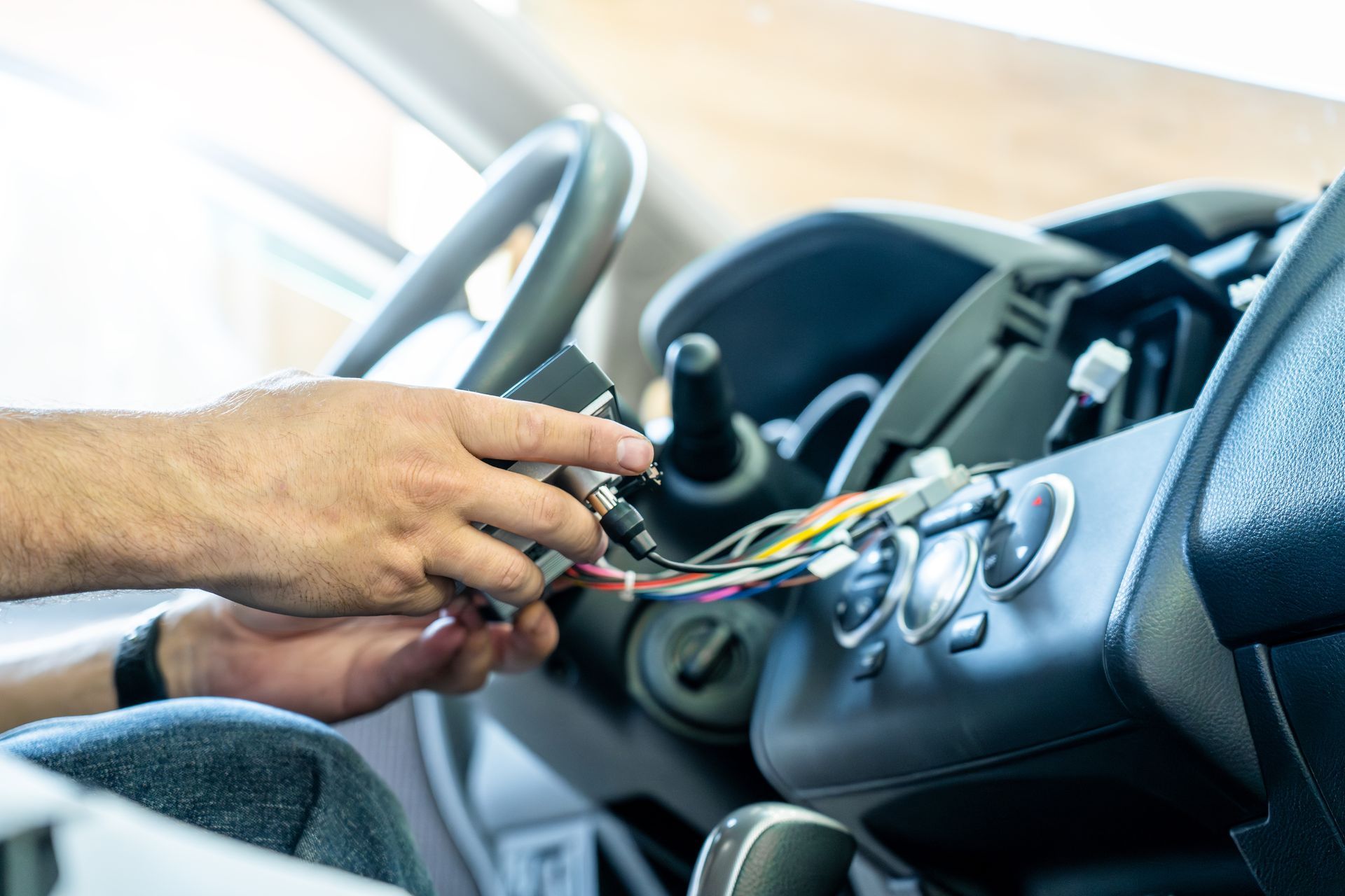 Person installing car stereo, connecting wires in vehicle dashboard.