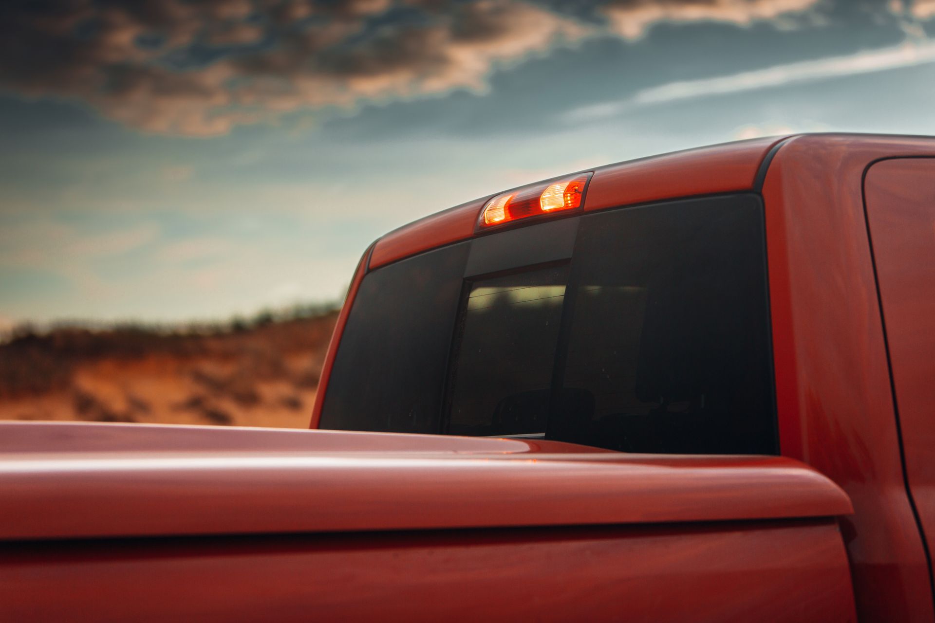 Red pickup truck bed and rear cab with a lit brake light against a desert landscape.