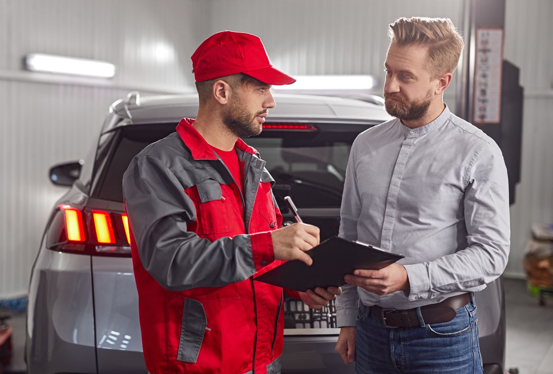 Mechanic in red overalls explains repairs to a customer in a car repair shop.