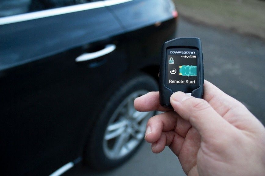 Hand holding car key fob near an open car door, poised to unlock it.