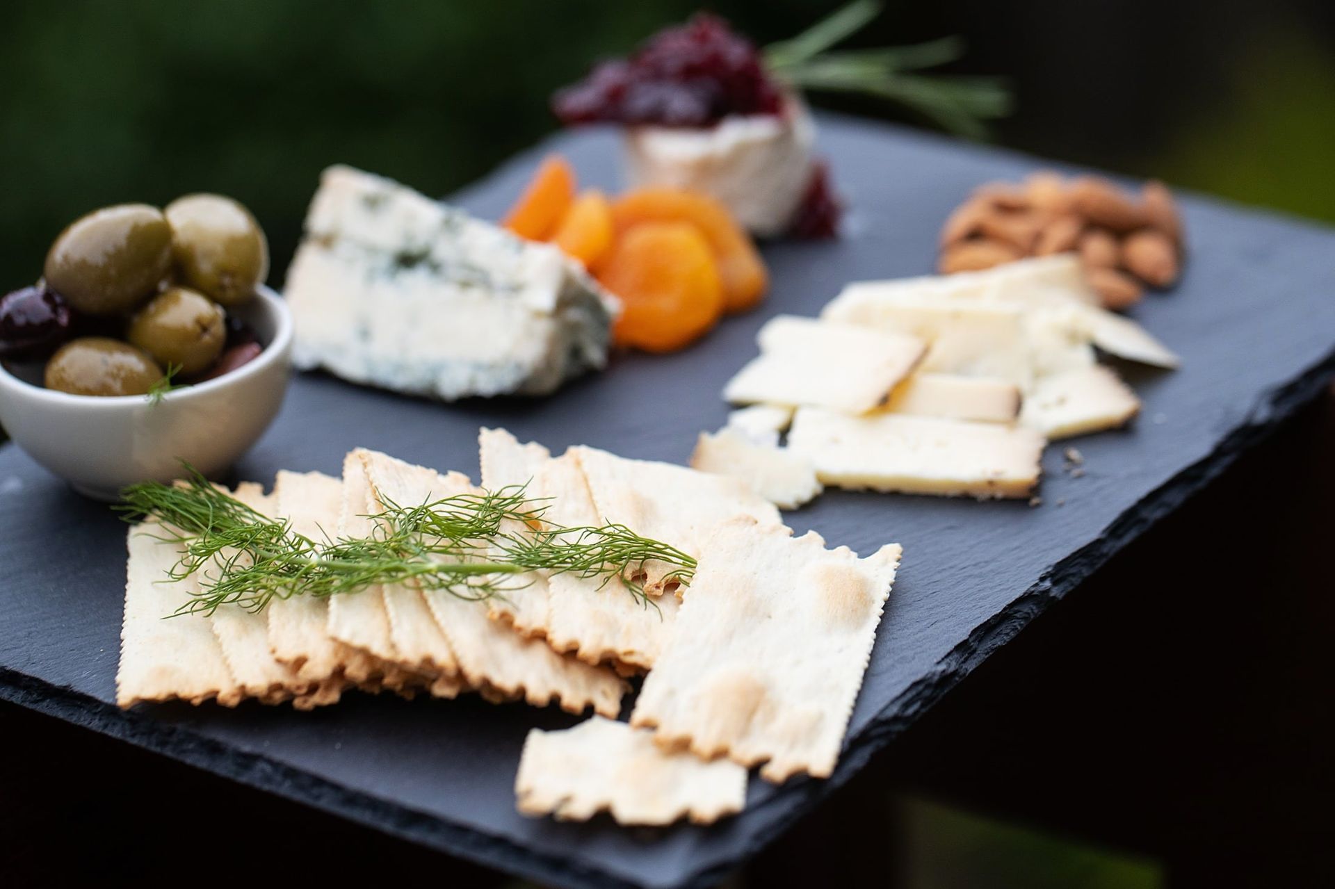 A tray of crackers , cheese , olives and nuts on a table.