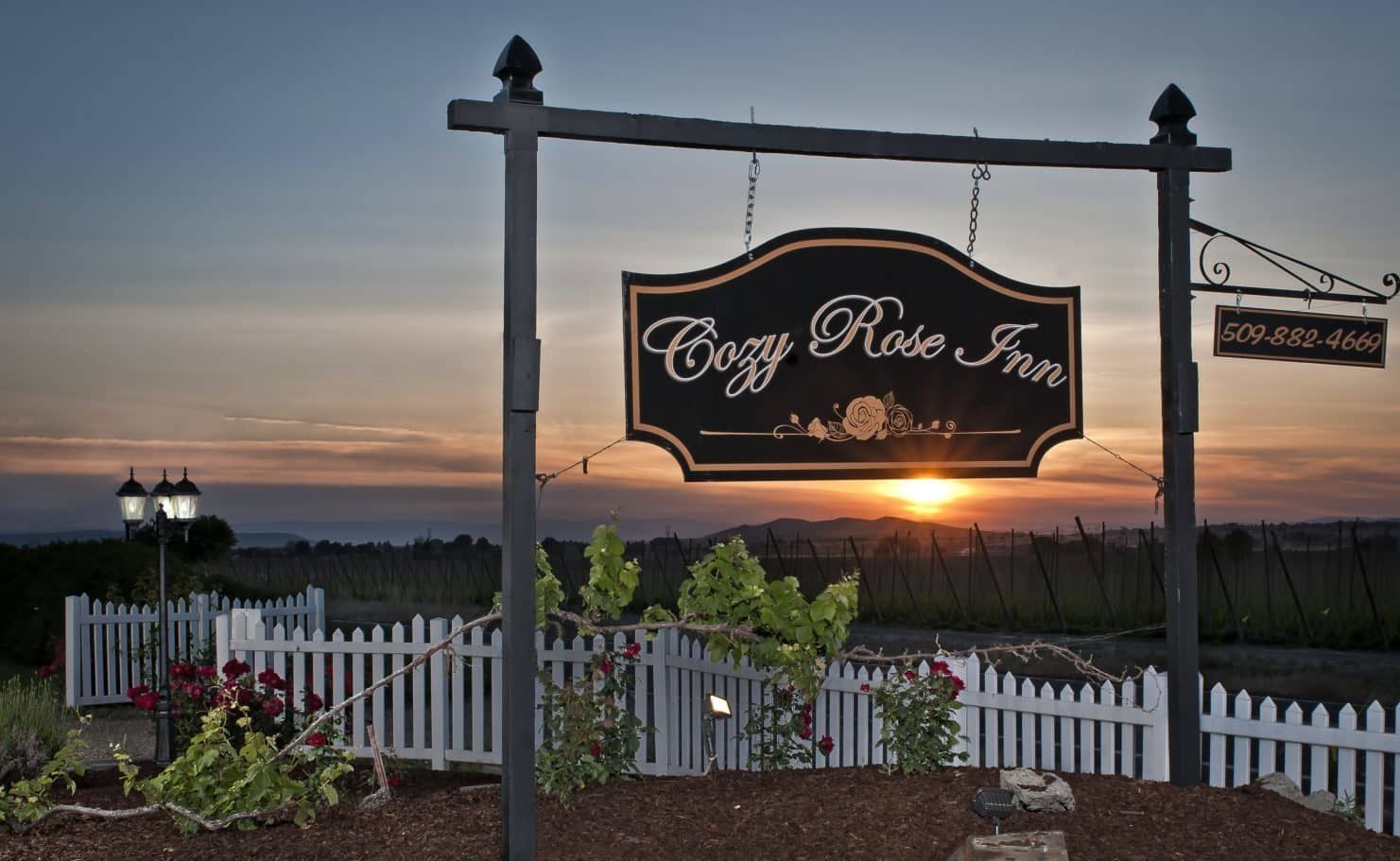 A sign for the cozy rose inn hangs above a white picket fence