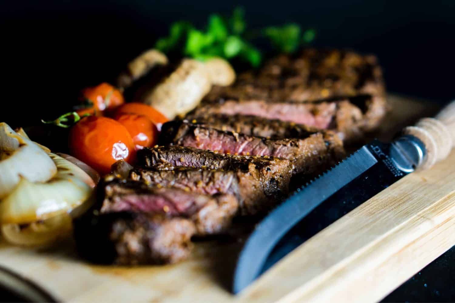 A close up of a steak on a cutting board with tomatoes and onions.