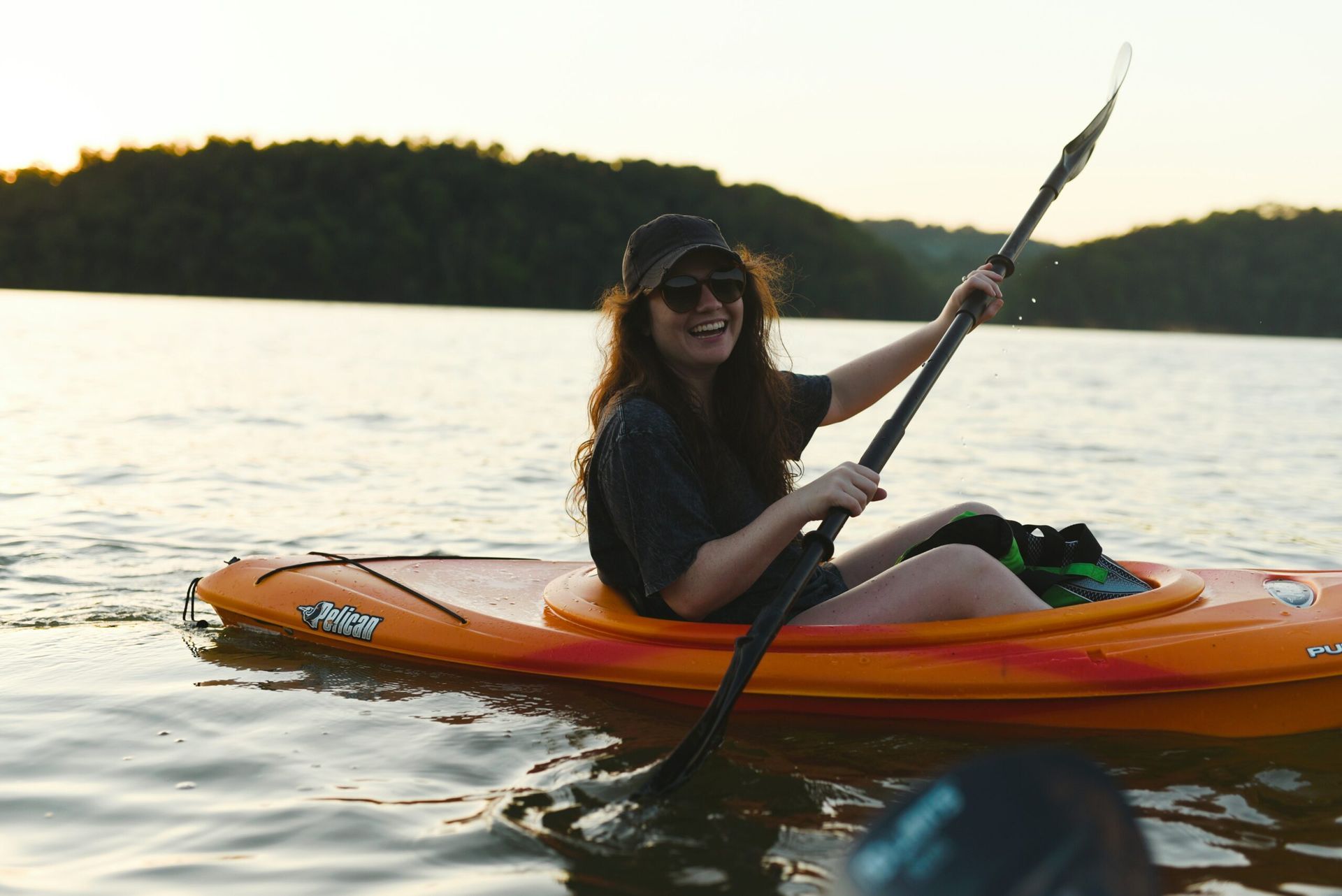 A woman is paddling an orange kayak on a lake.