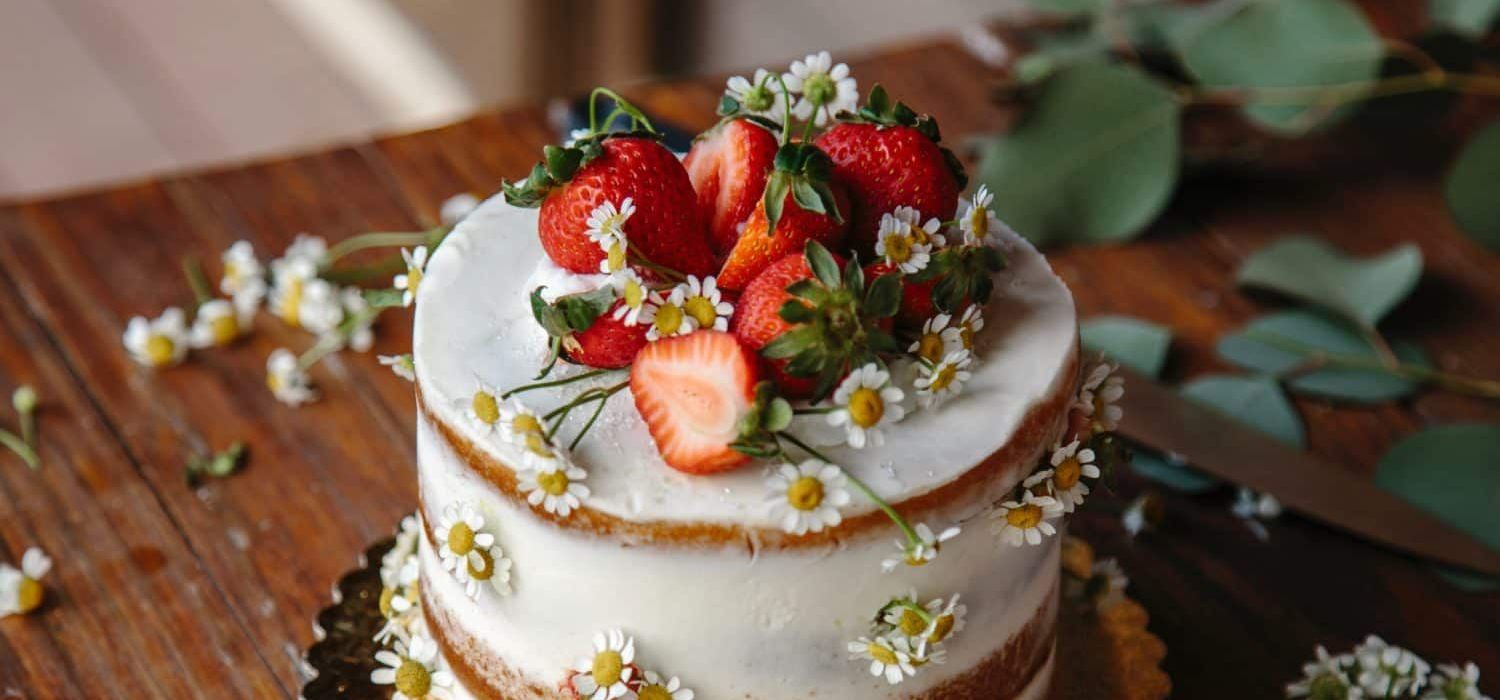 A cake with strawberries and daisies on top of it on a wooden table.