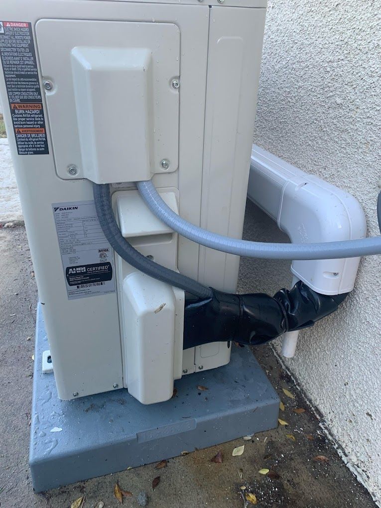 A white air conditioner is sitting on top of a concrete base next to a wall.