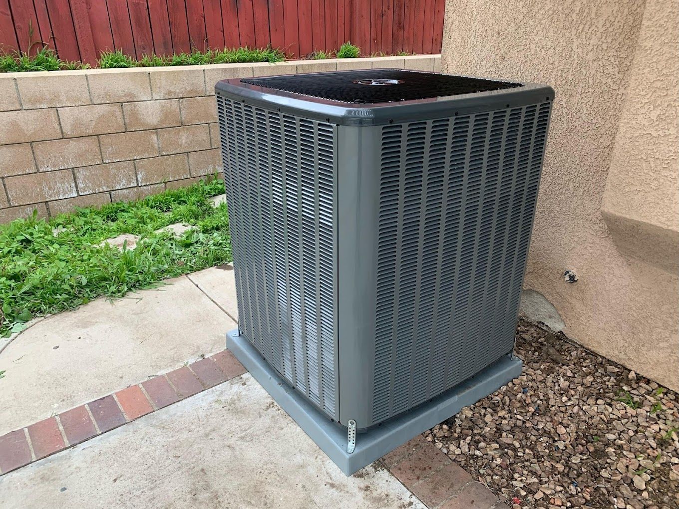 A gray air conditioner is sitting on the side of a building.