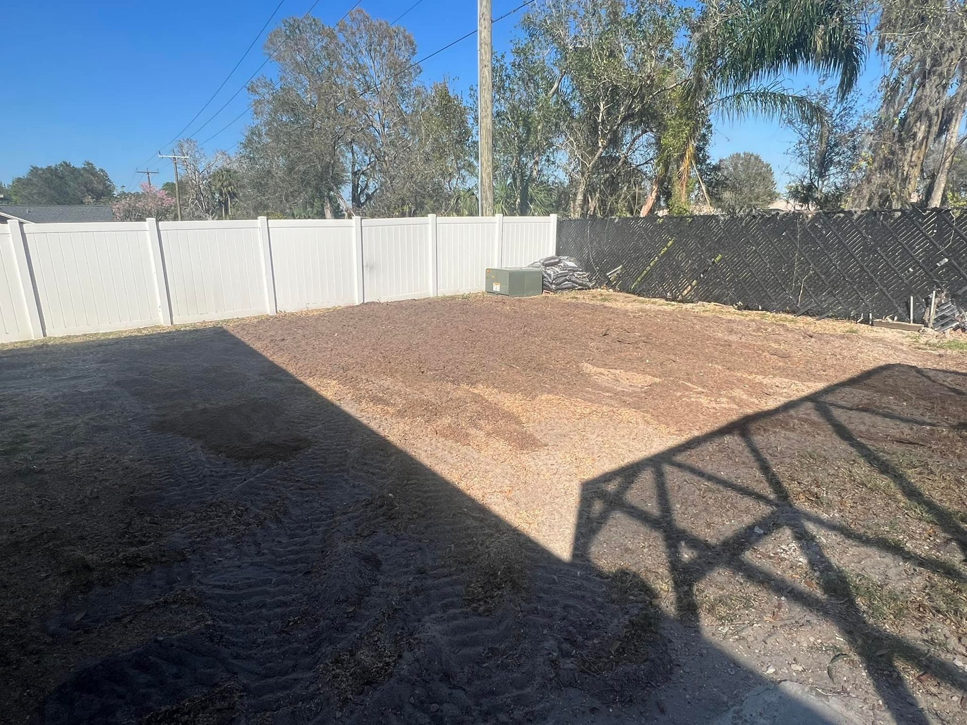 A backyard with a white fence and trees in the background.