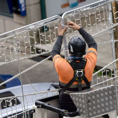 Elite Insta Bros Designs llc - Worker in orange shirt and hardhat installing Christmas lights from a lift.