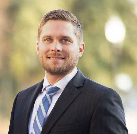 Dustin Galmor in a suit and tie is smiling for the camera.