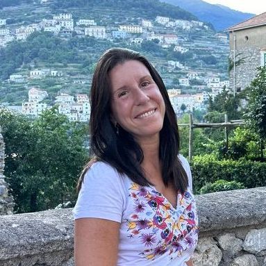 Una mujer está sentada en un muro de piedra frente a una montaña.