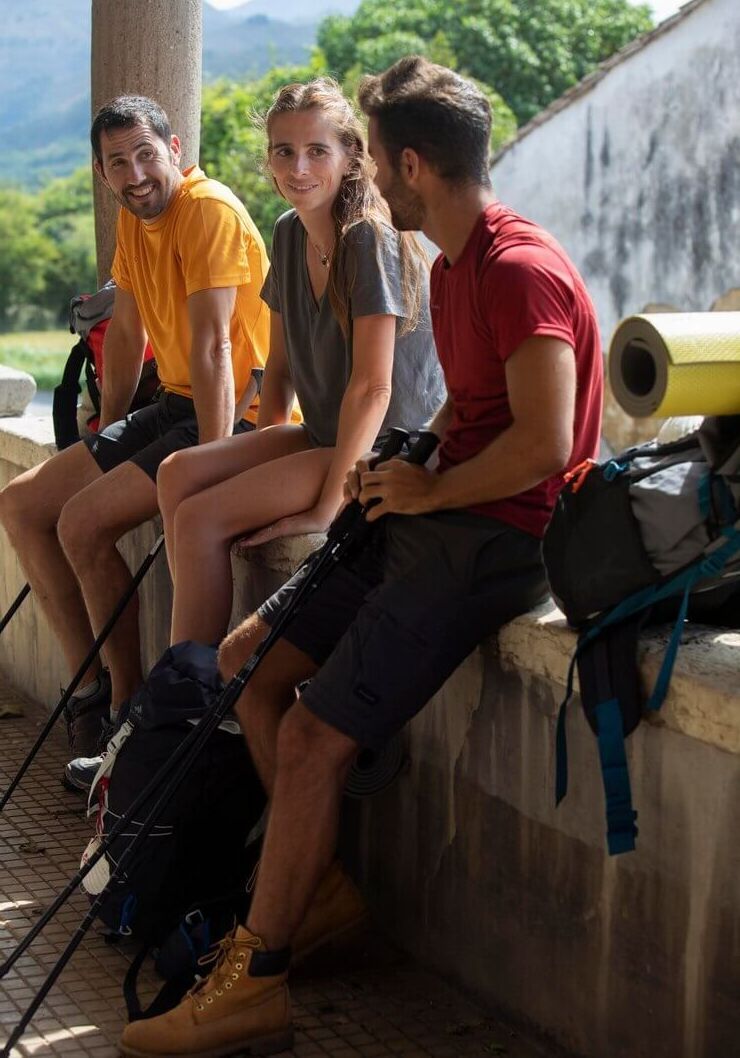 Un grupo de personas está sentada en una pared con mochilas.