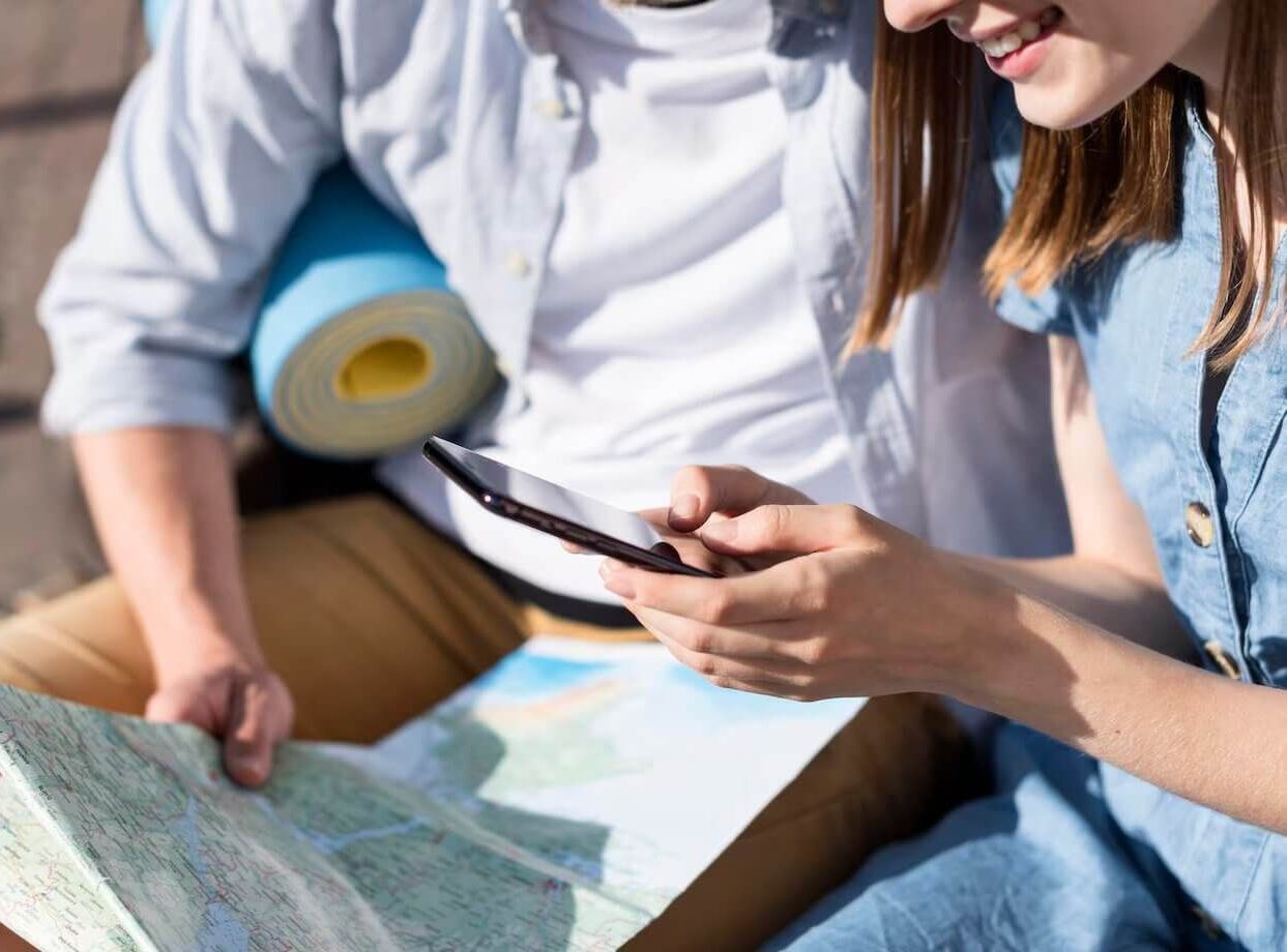 Un hombre y una mujer están sentados uno al lado del otro mirando un mapa y un teléfono celular.