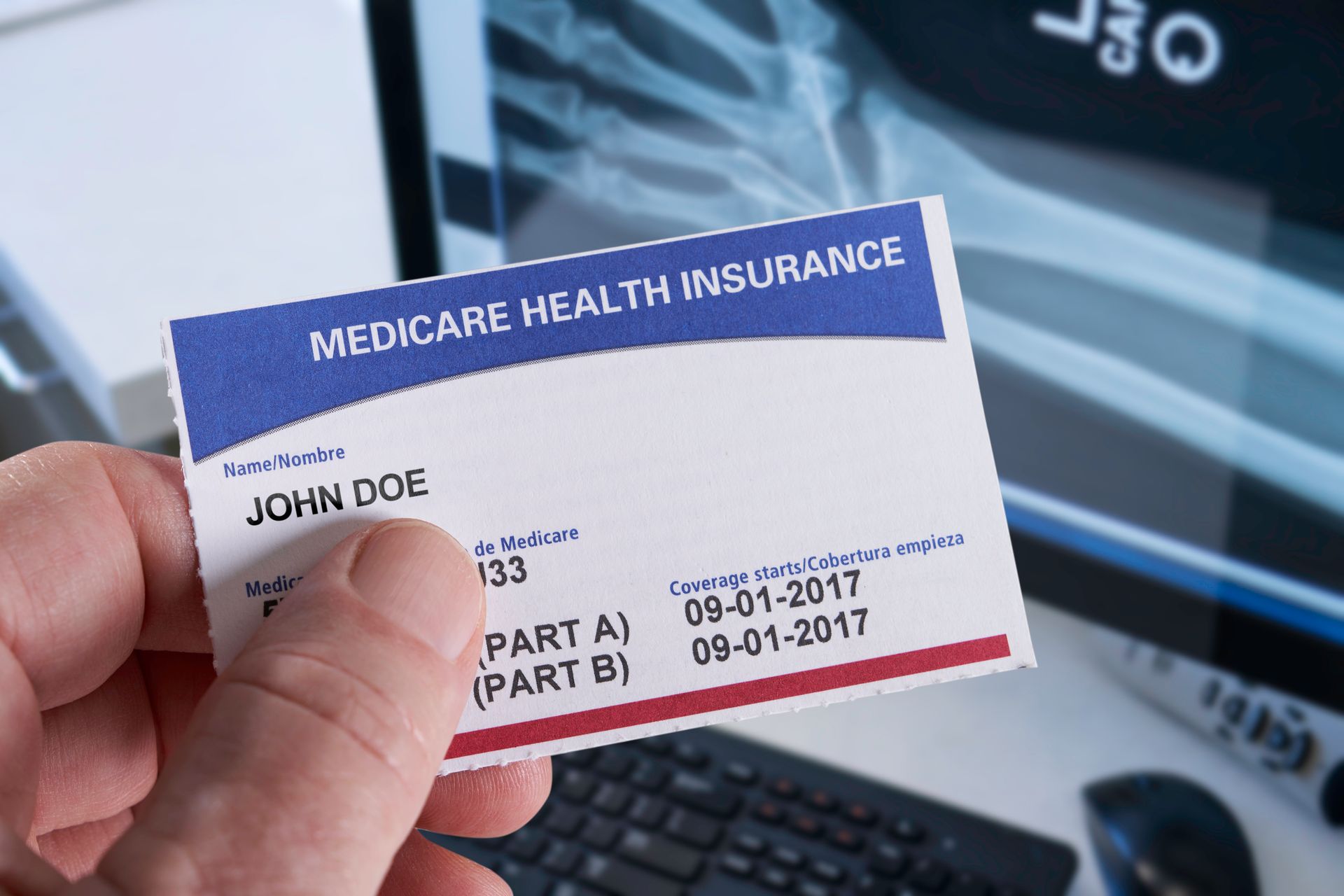Medicare insurance card in hand at a medical office, with an X-ray in the background.