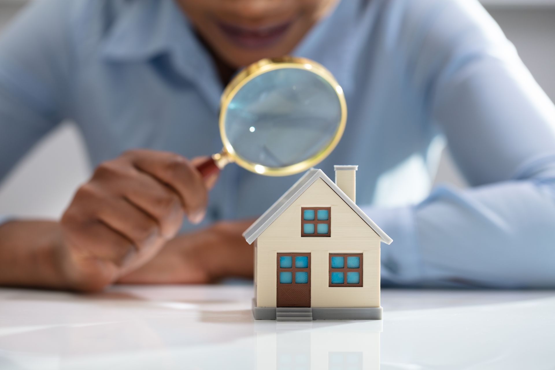 A woman is looking at a model house through a magnifying glass.