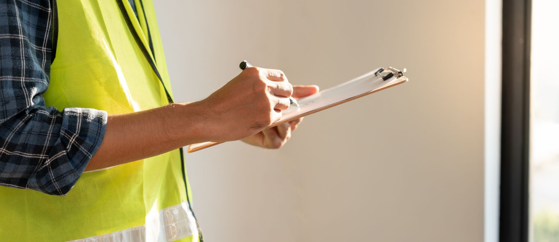 A man in a yellow vest is holding a clipboard and writing on it.