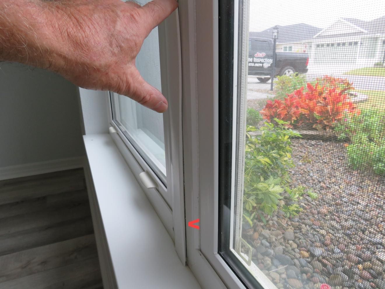 A hand points to a detached or loose piece of interior white window trim, highlighting a gap in the frame.