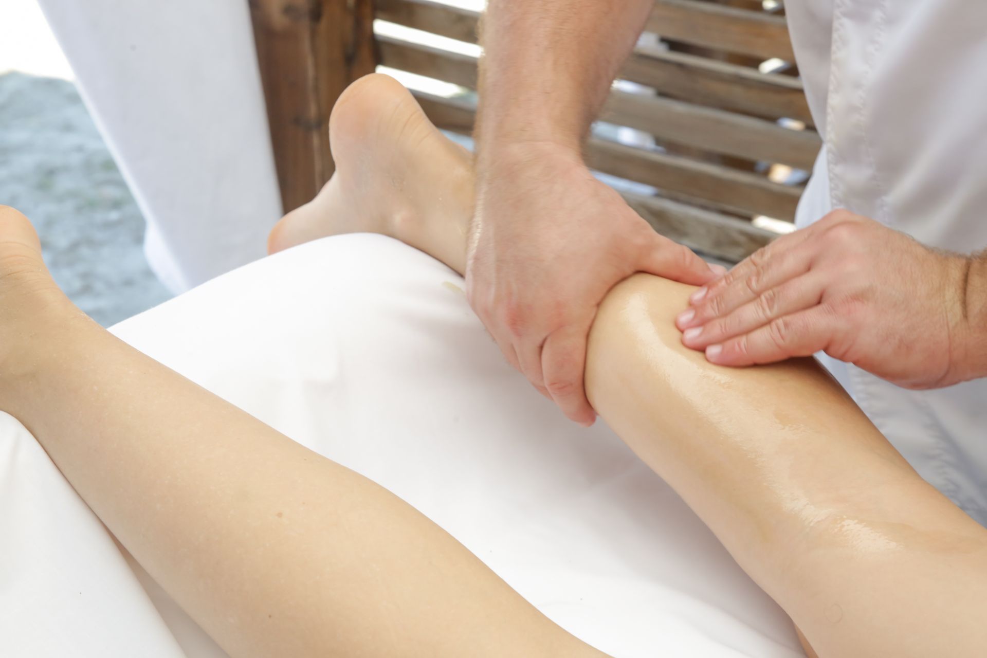 A therapist provides a calf massage on a person's lower leg, which is resting on a white massage table.