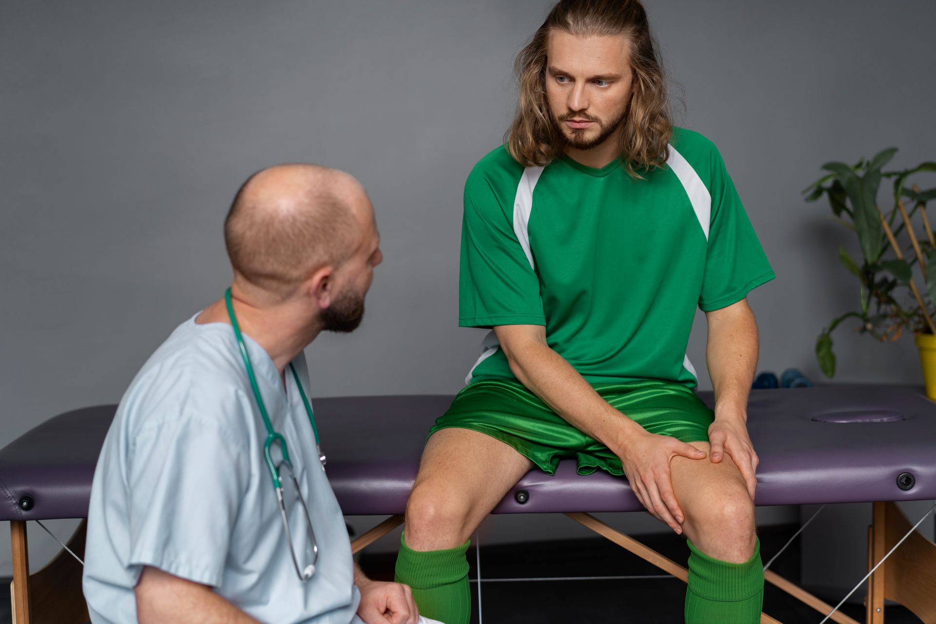 Doctor examines soccer player's injured knee; green uniform, medical setting, pained expression.