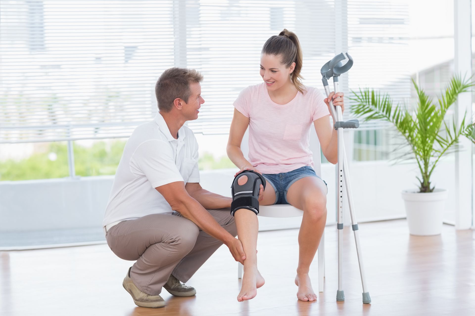 A man is helping a woman with crutches and knee braces.