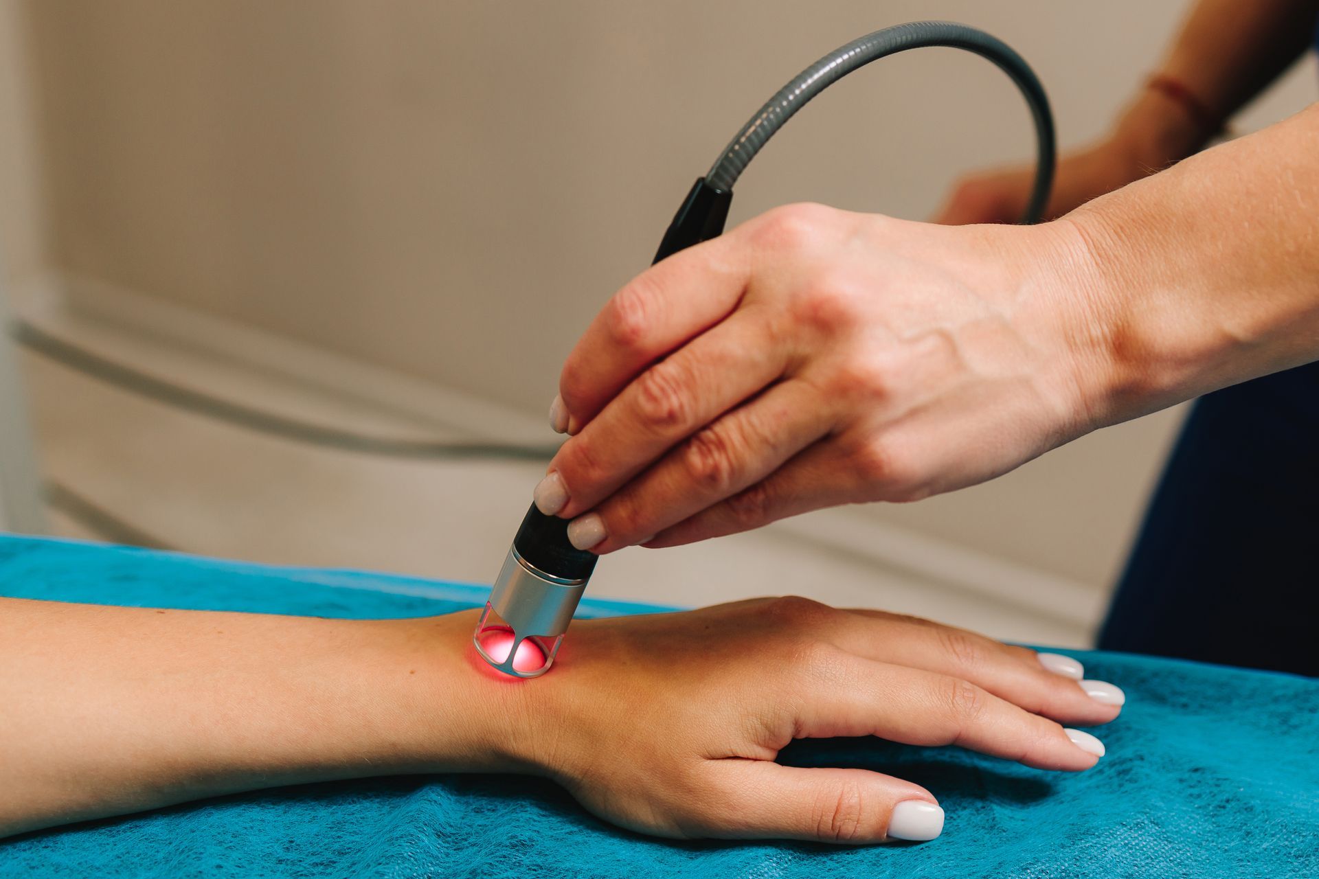 Hand receiving laser therapy treatment on wrist. A pink laser light is visible.