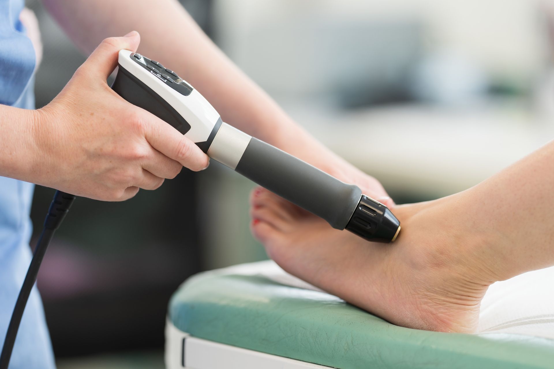 A medical professional using a device on a patient's ankle in a clinic setting.