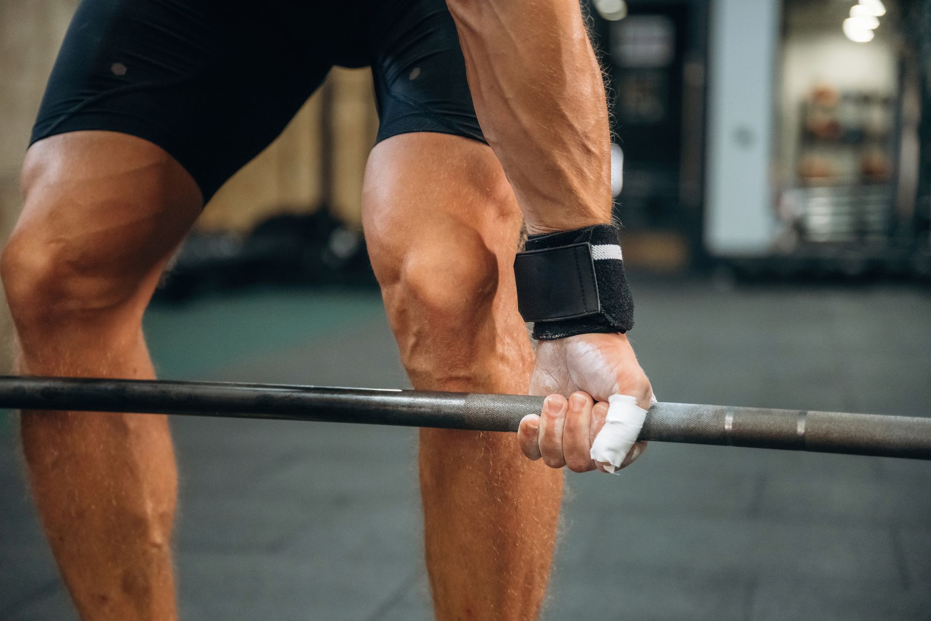 Person lifting a barbell with chalked hands, wearing wrist wraps and shorts, in a gym.