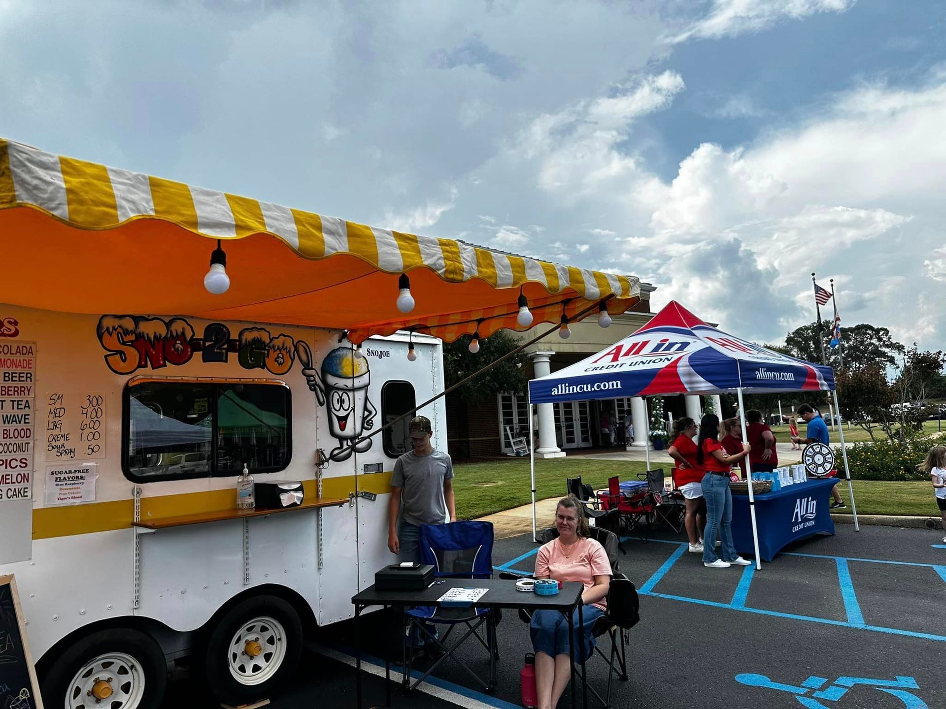 A woman is sitting at a table in front of an ice cream truck.