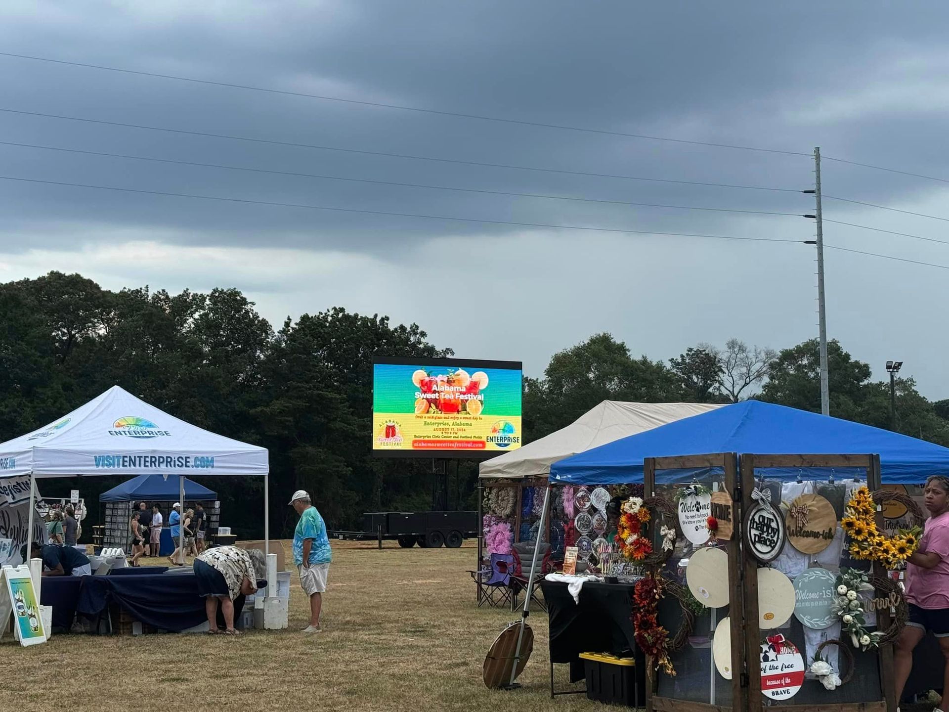 A group of people are standing in a field with tents and a large screen