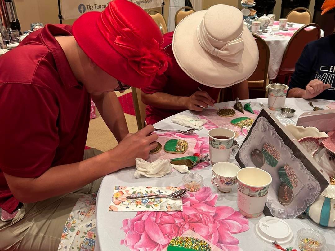 Two people wearing hats are sitting at a table decorating cookies.