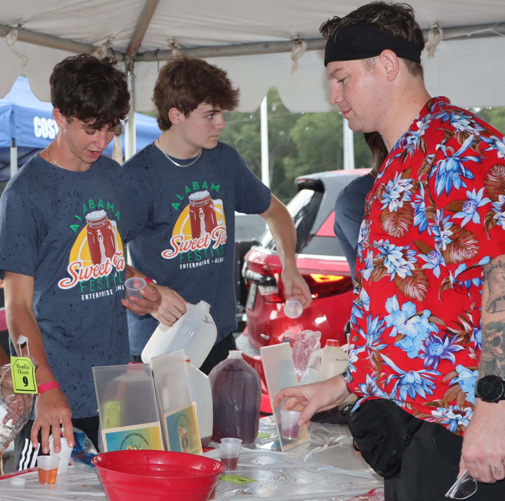 A man in a floral shirt is pouring a drink into a cup