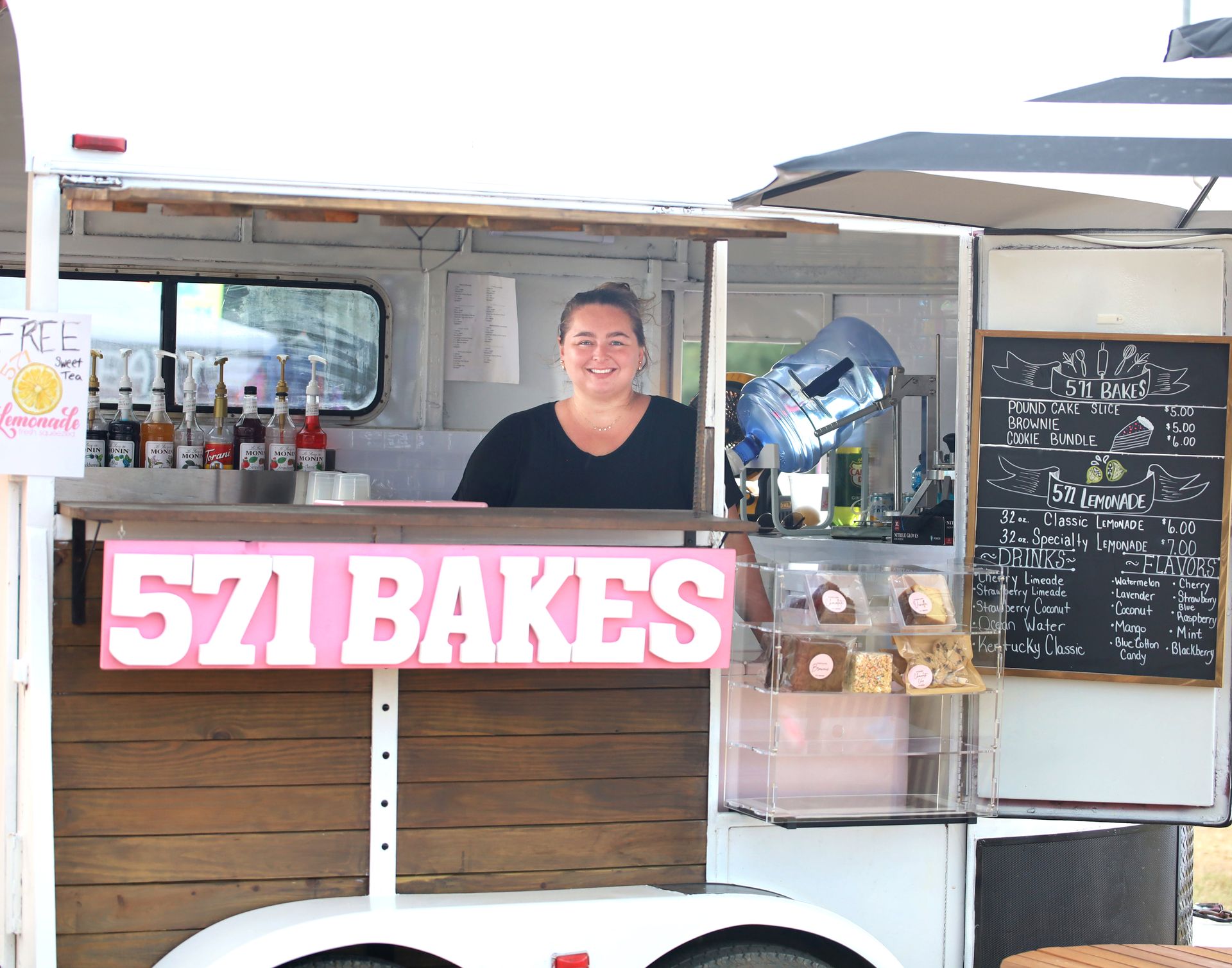 A woman is behind a counter in a food truck that says 571 bakes