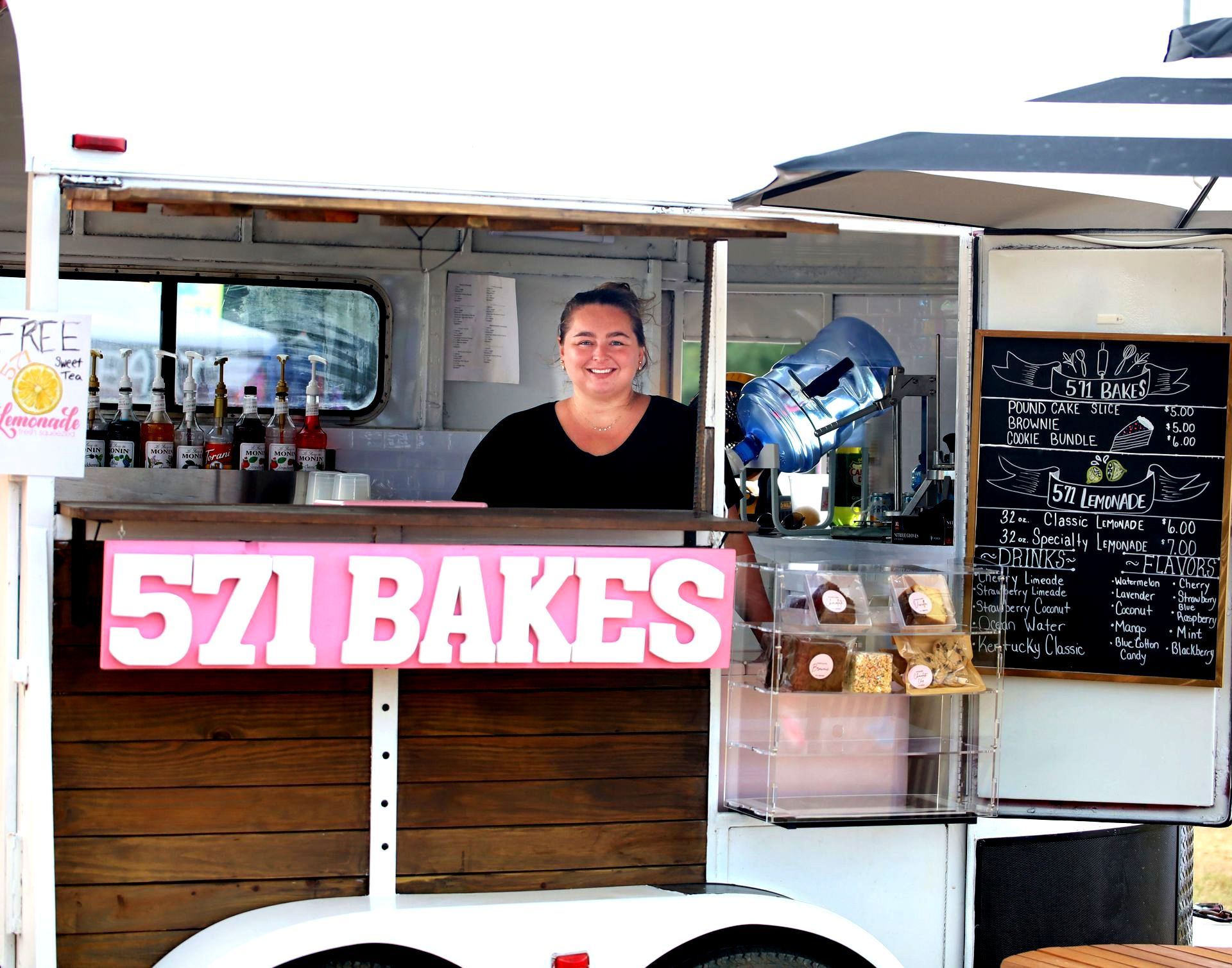 A woman is behind a counter in a food truck that says 571 bakes