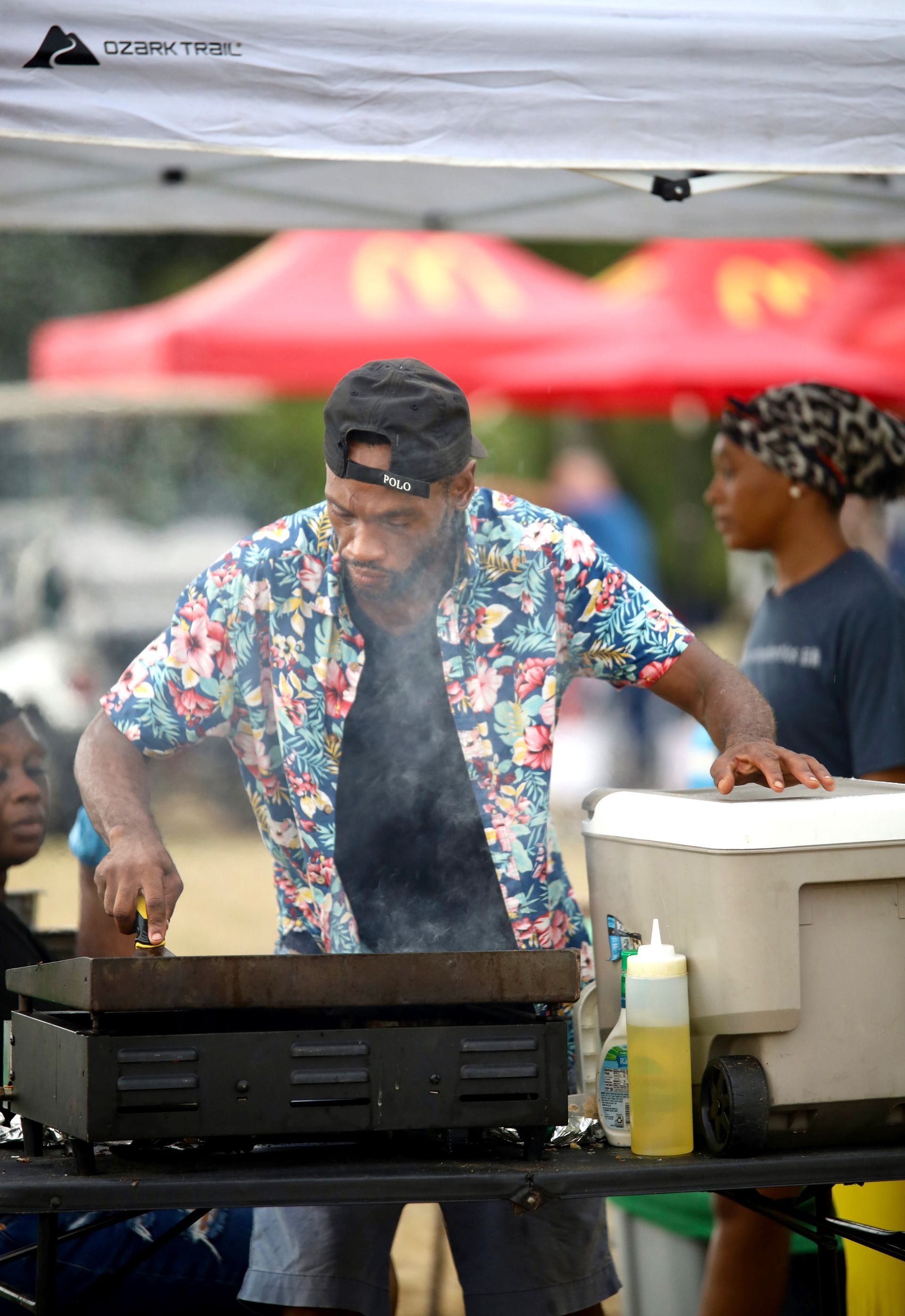A man in a floral shirt is cooking food on a grill.