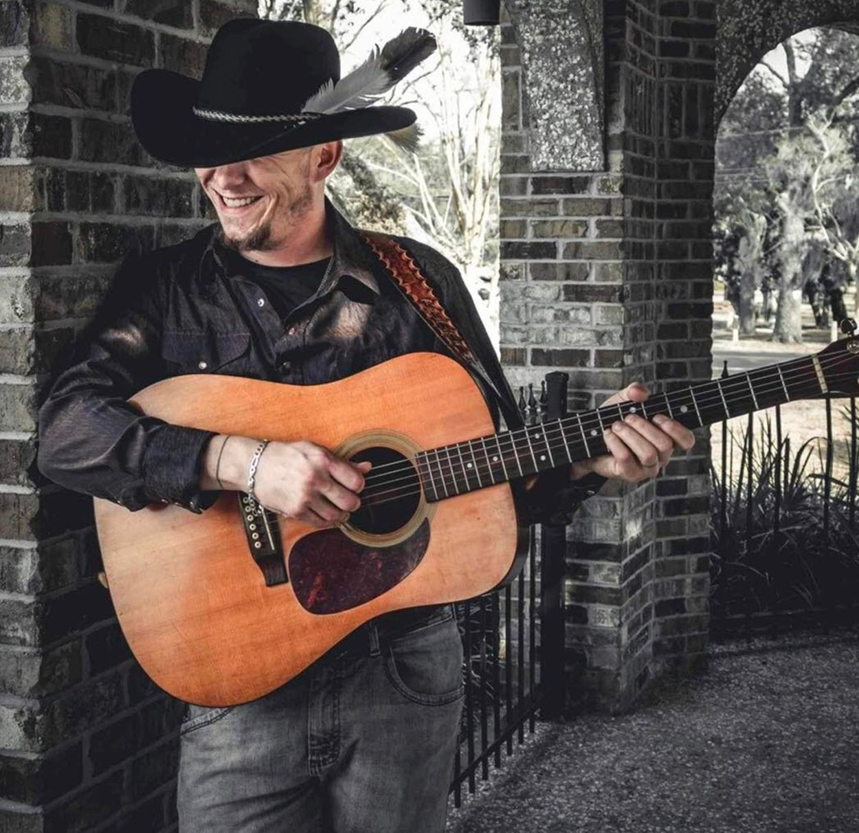 A man wearing a cowboy hat is playing an acoustic guitar