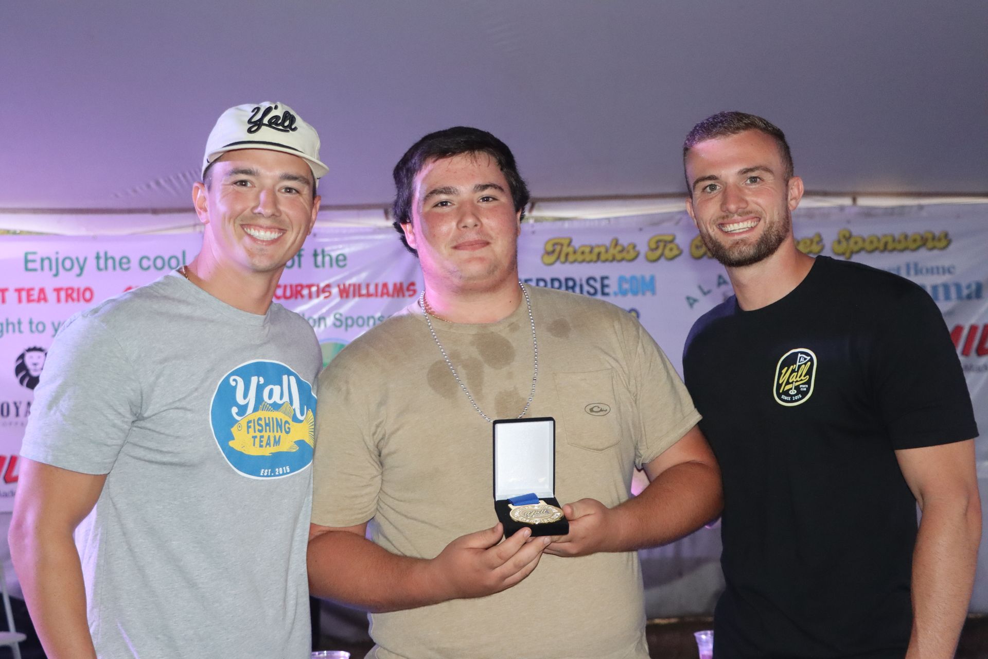 Three men are posing for a picture and one of them is holding a medal