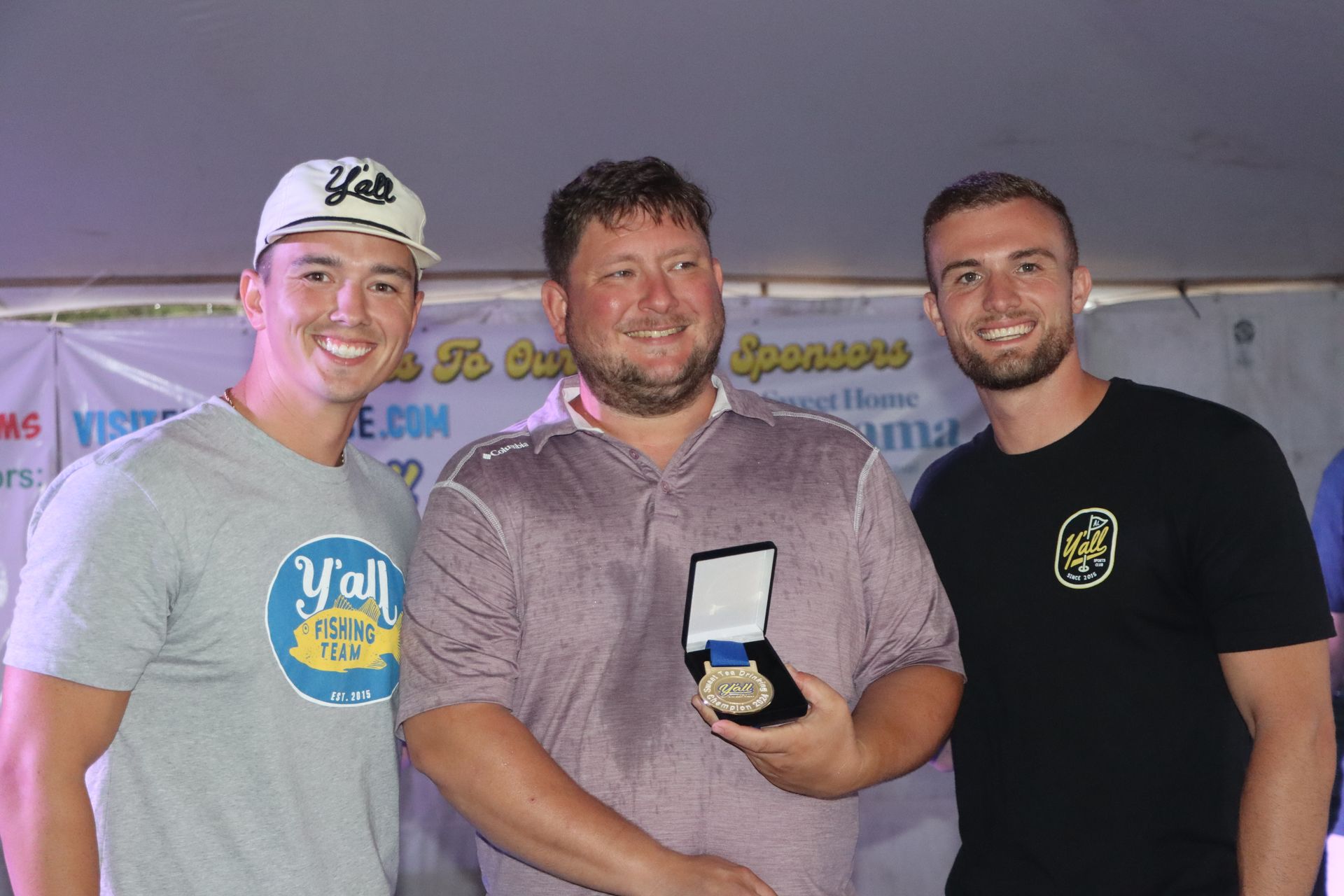 Three men are standing next to each other and one of them is holding a medal.