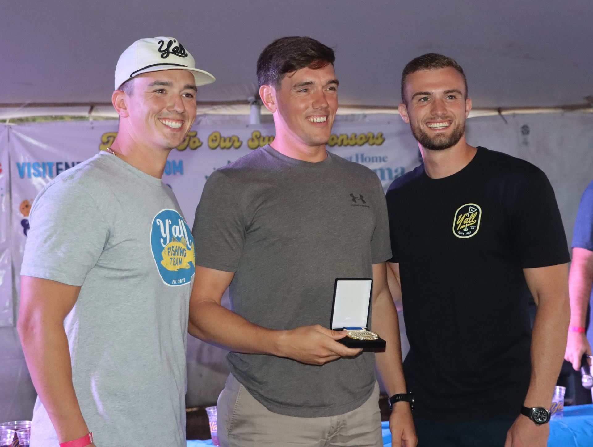 Three men are posing for a picture and one of them is holding a trophy