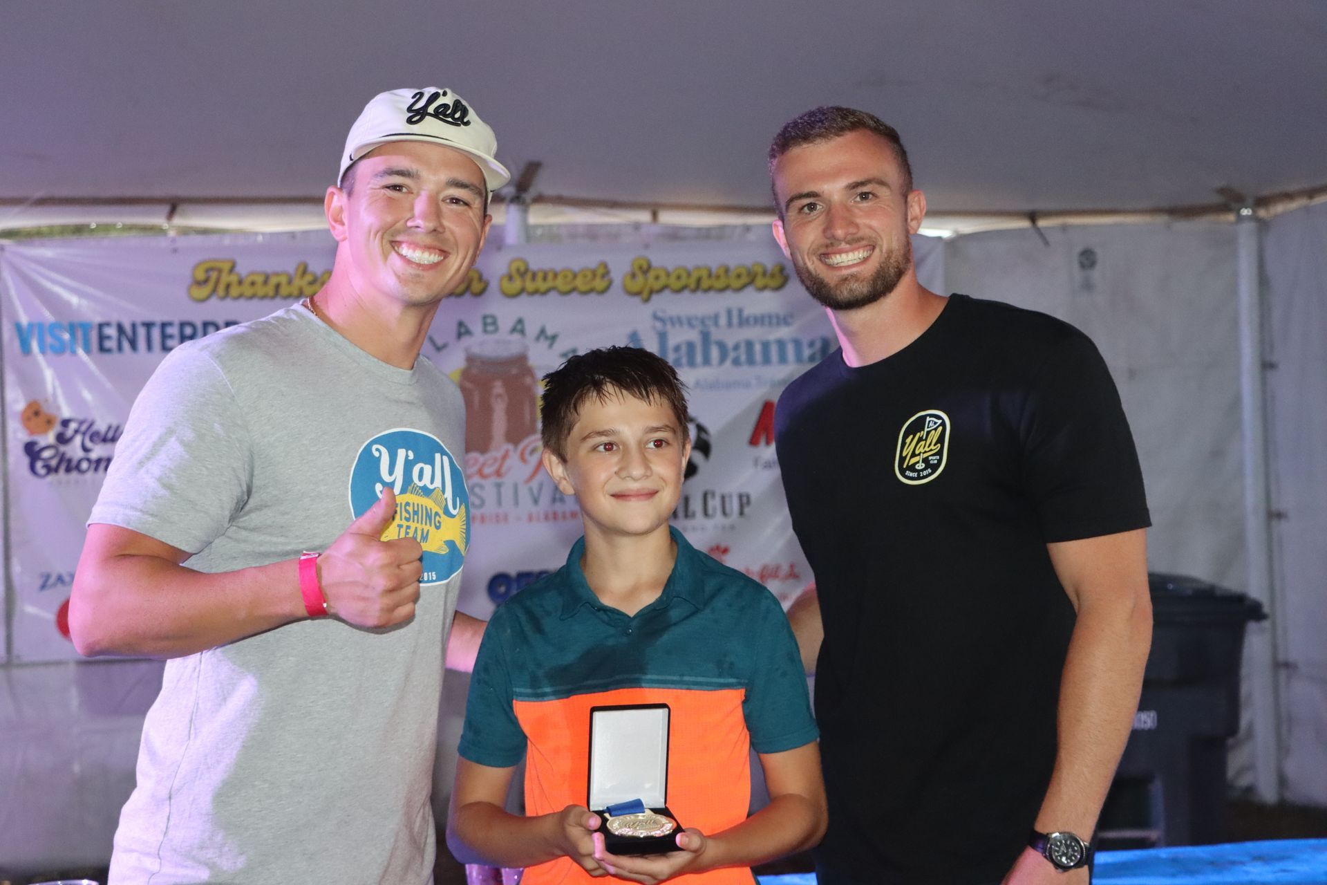 Three men are posing for a picture with a young boy holding a medal.