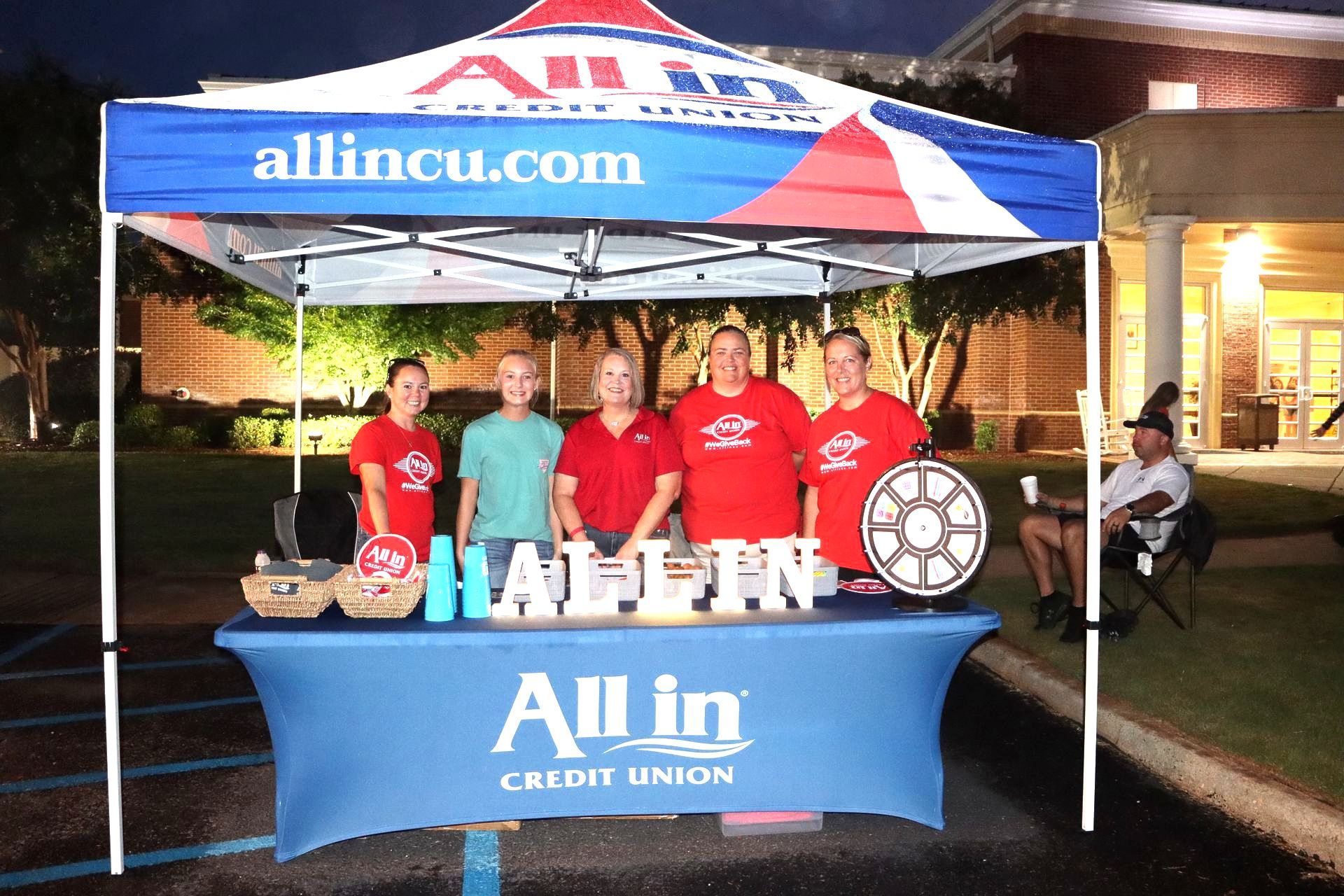 A group of people standing under an all in credit union tent