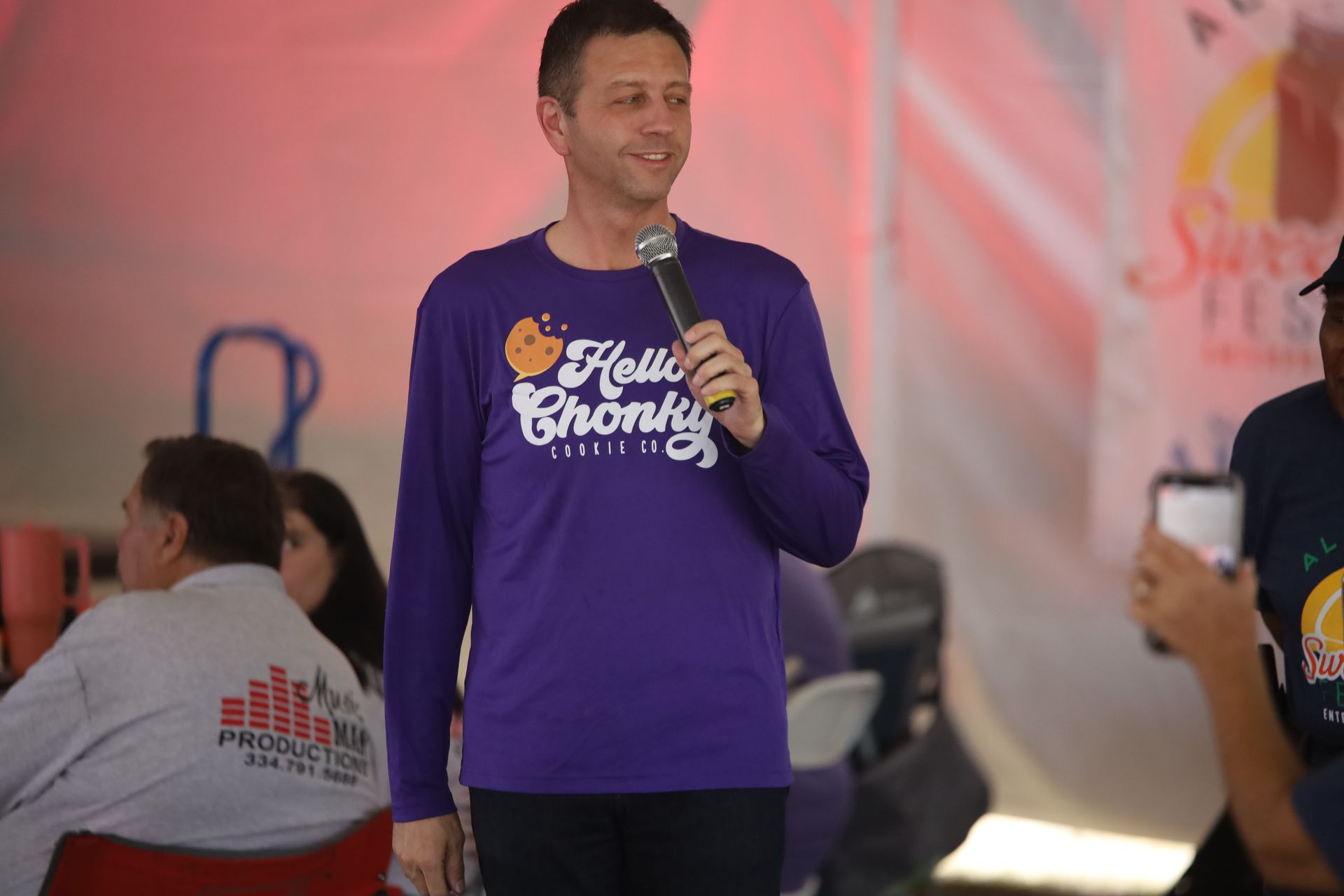 A man wearing a purple shirt that says hello chunky is holding a microphone.