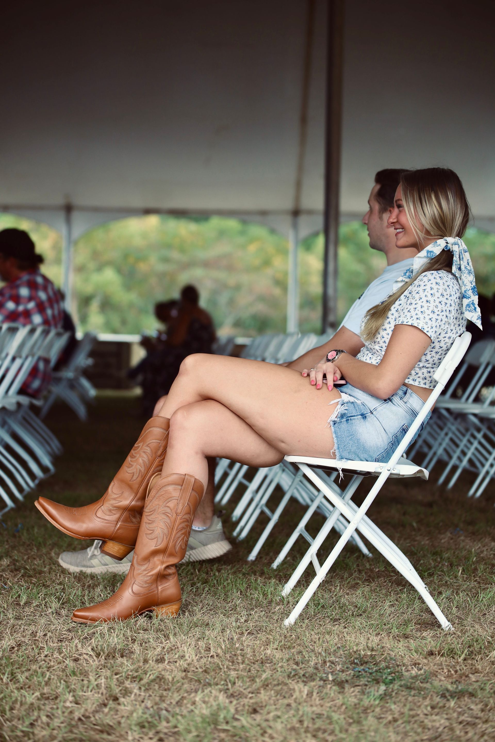 A woman wearing cowboy boots is sitting in a white folding chair.
