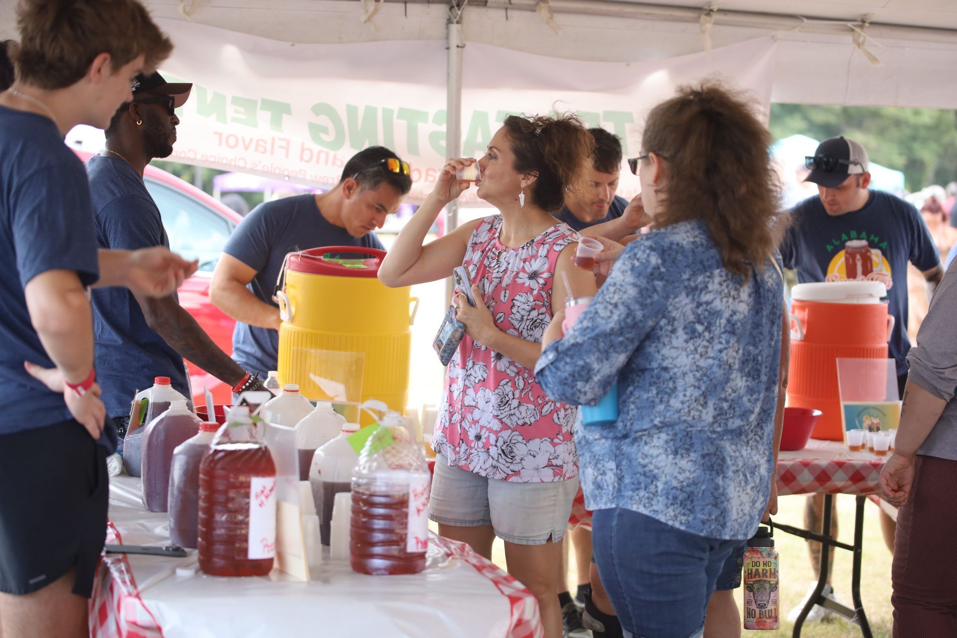 A group of people are standing around a table with bottles of liquid on it.