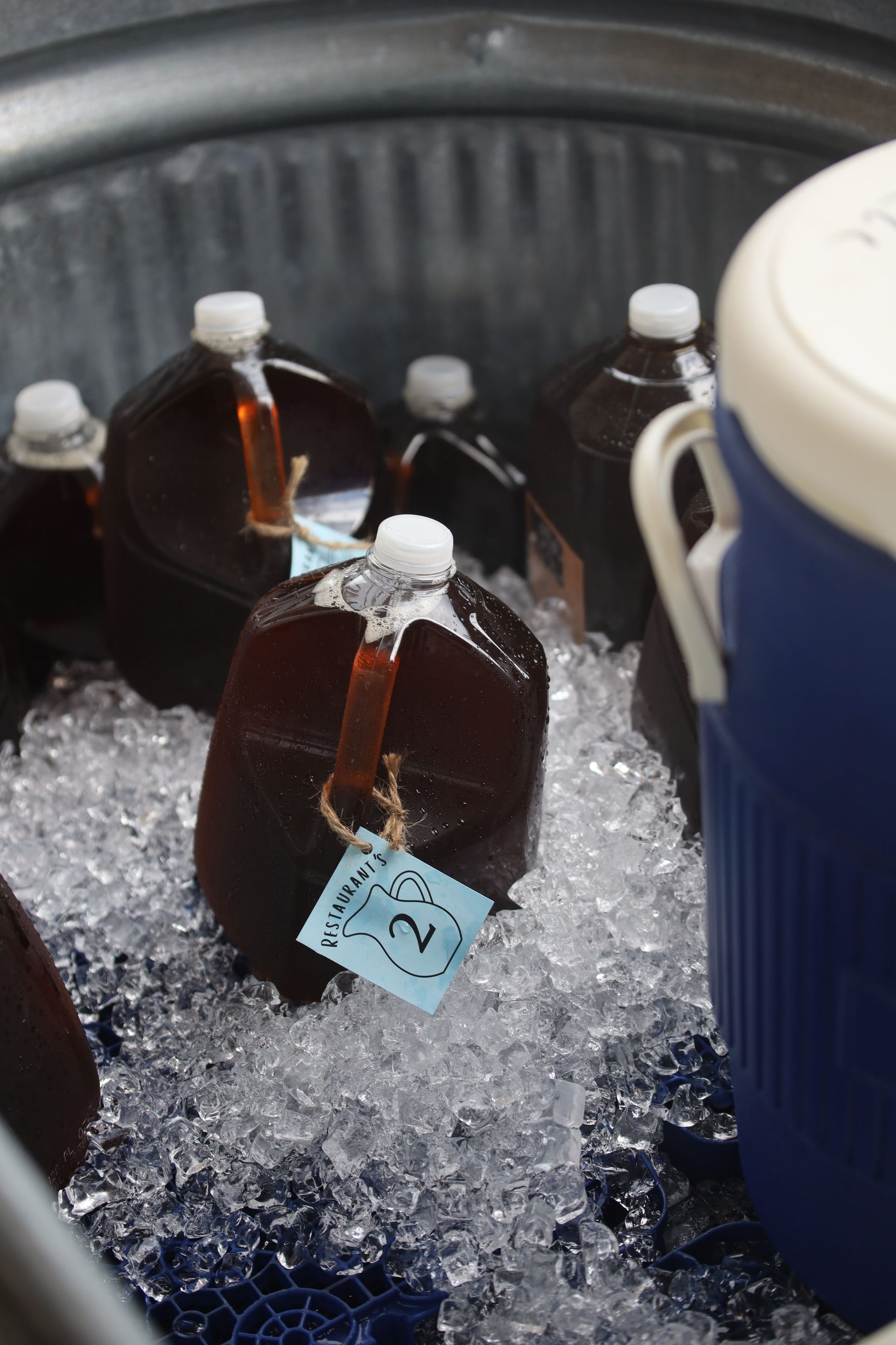 Several bottles of syrup are sitting in a bucket of ice.