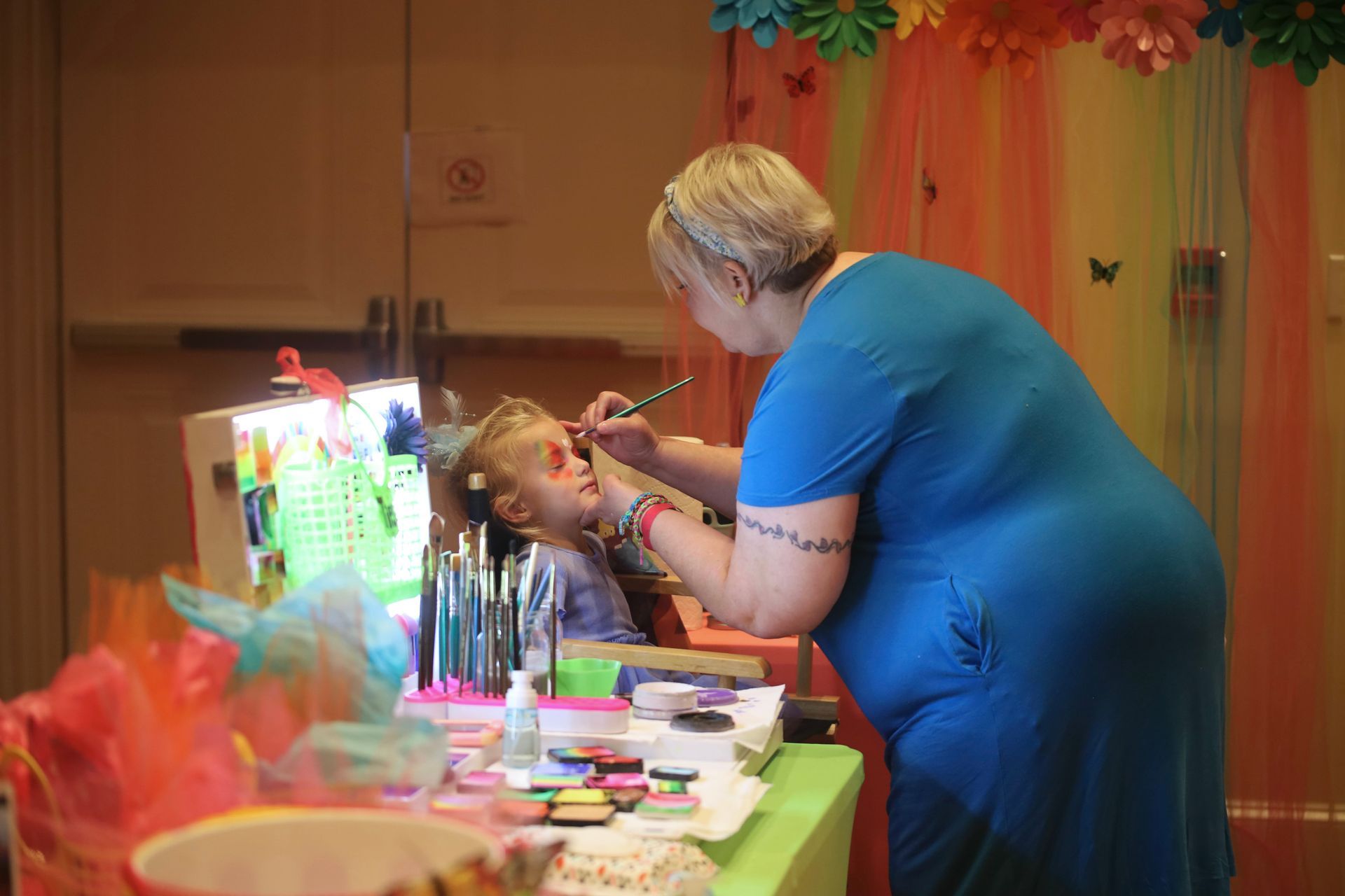 A woman is painting a child 's face at a party.