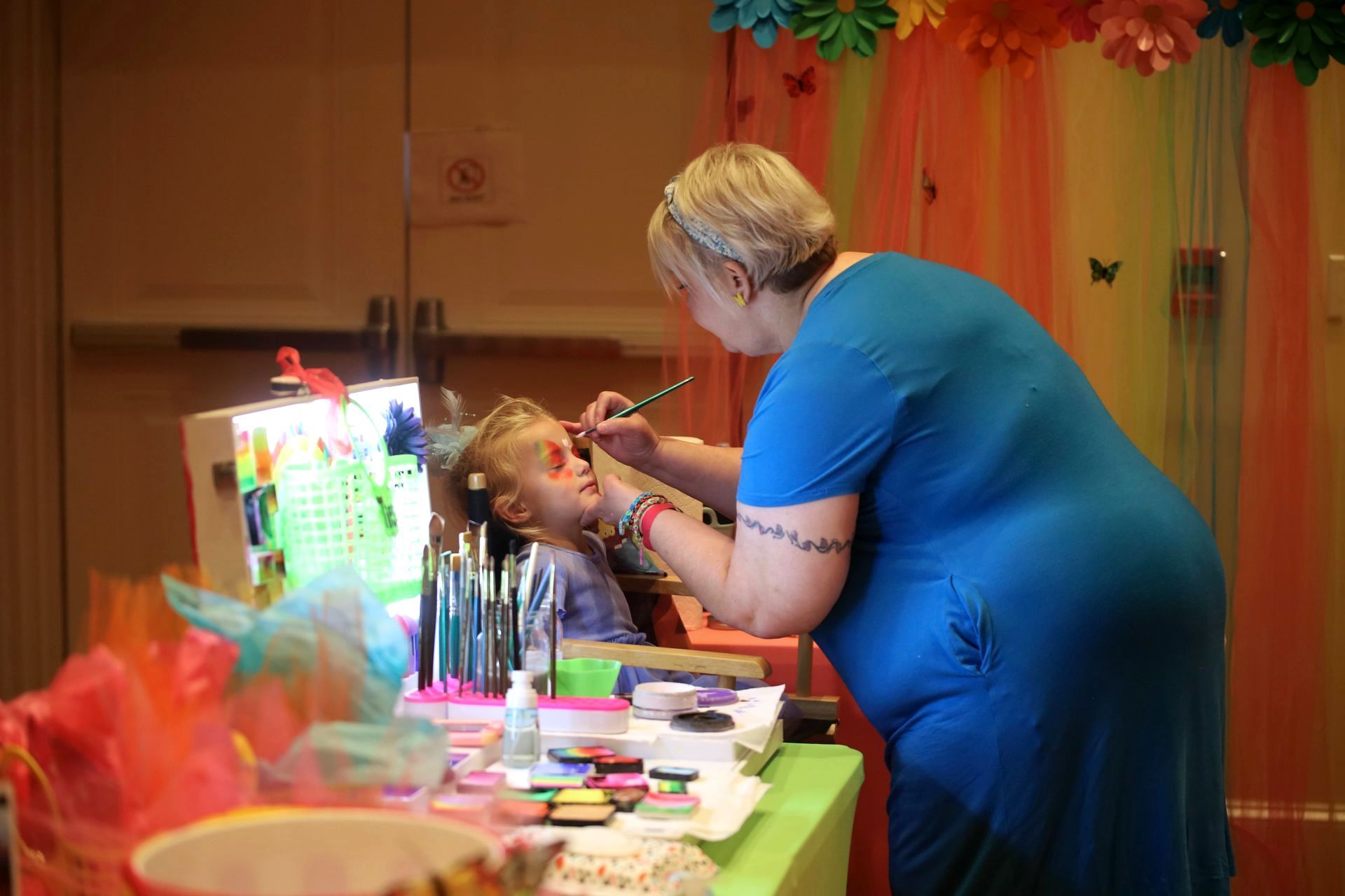 A woman is painting a child 's face at a party.