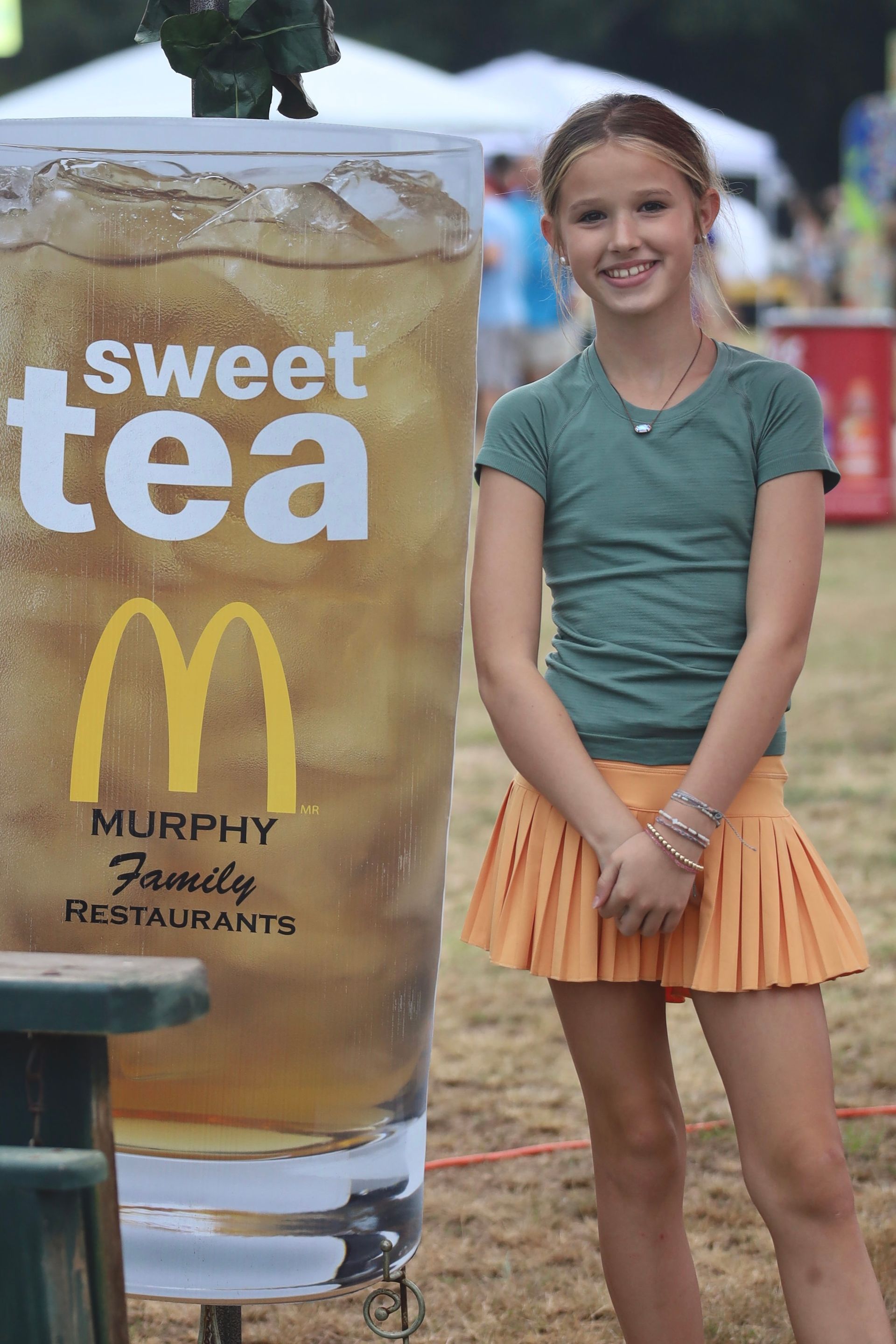 A young girl is standing in front of a mcdonald 's sweet tea sign.